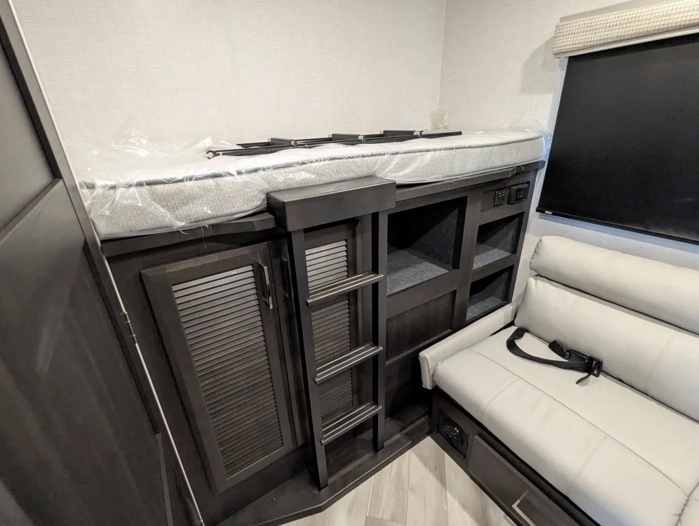 2026 Holiday Rambler Invicta 36Y — Overhead bunk mattress and ladder above storage cabinetry beside part of the living-room sofa