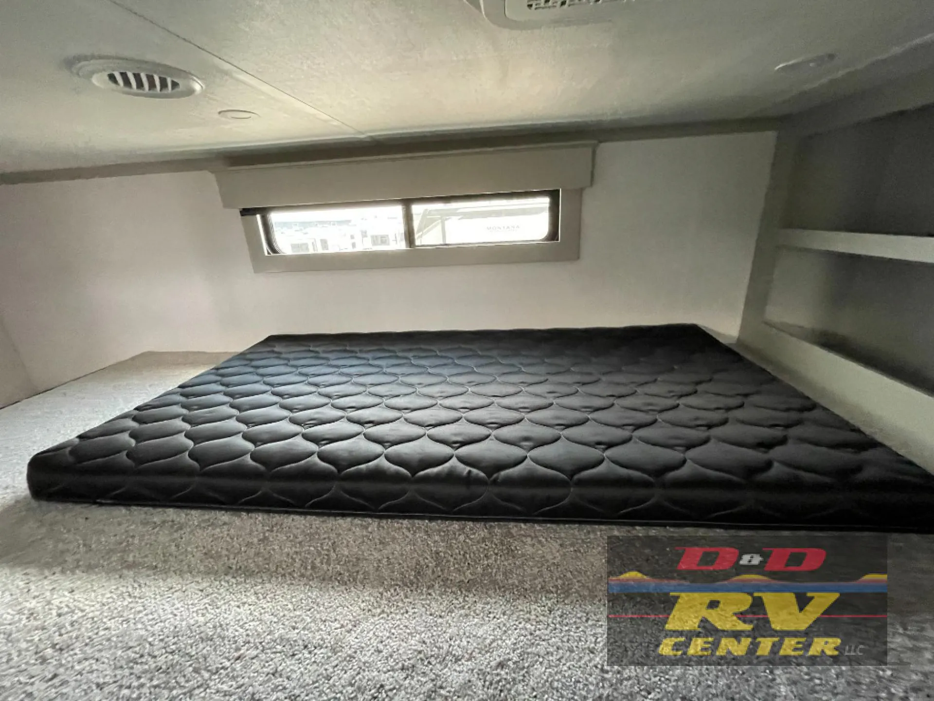 2026 Keystone Montana High Country 377FL — Black mattress fills an elevated sleeping loft beneath a window, with carpeted floor and built-in side shelves