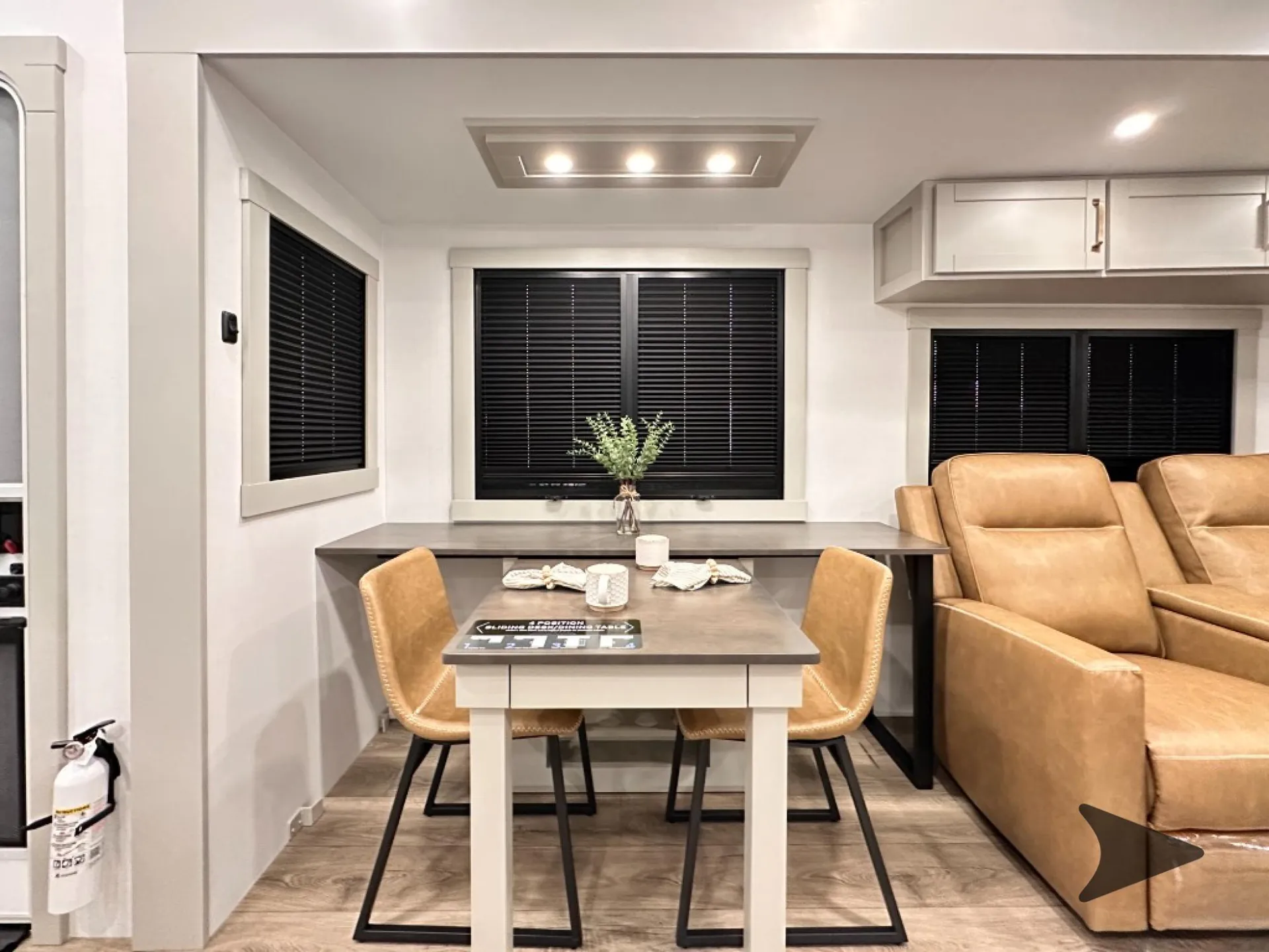 2026 Brinkley Model Z 3610 — RV dining table with four chairs beside two tan lounge recliners and surrounding windows