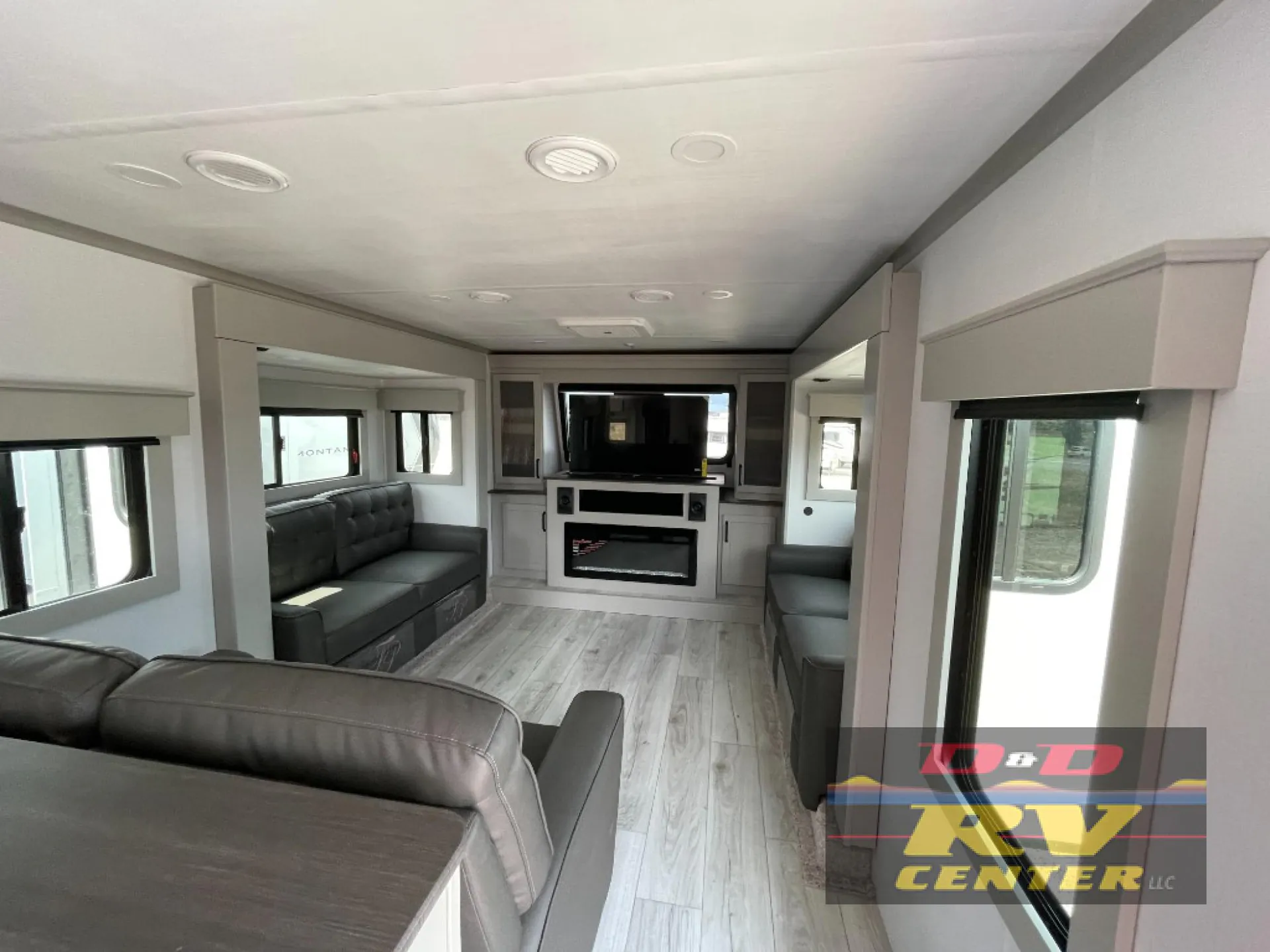 2026 Keystone Montana High Country 377FL — Fifth-wheel living room with sofa, recliners, television, fireplace, and surrounding windows