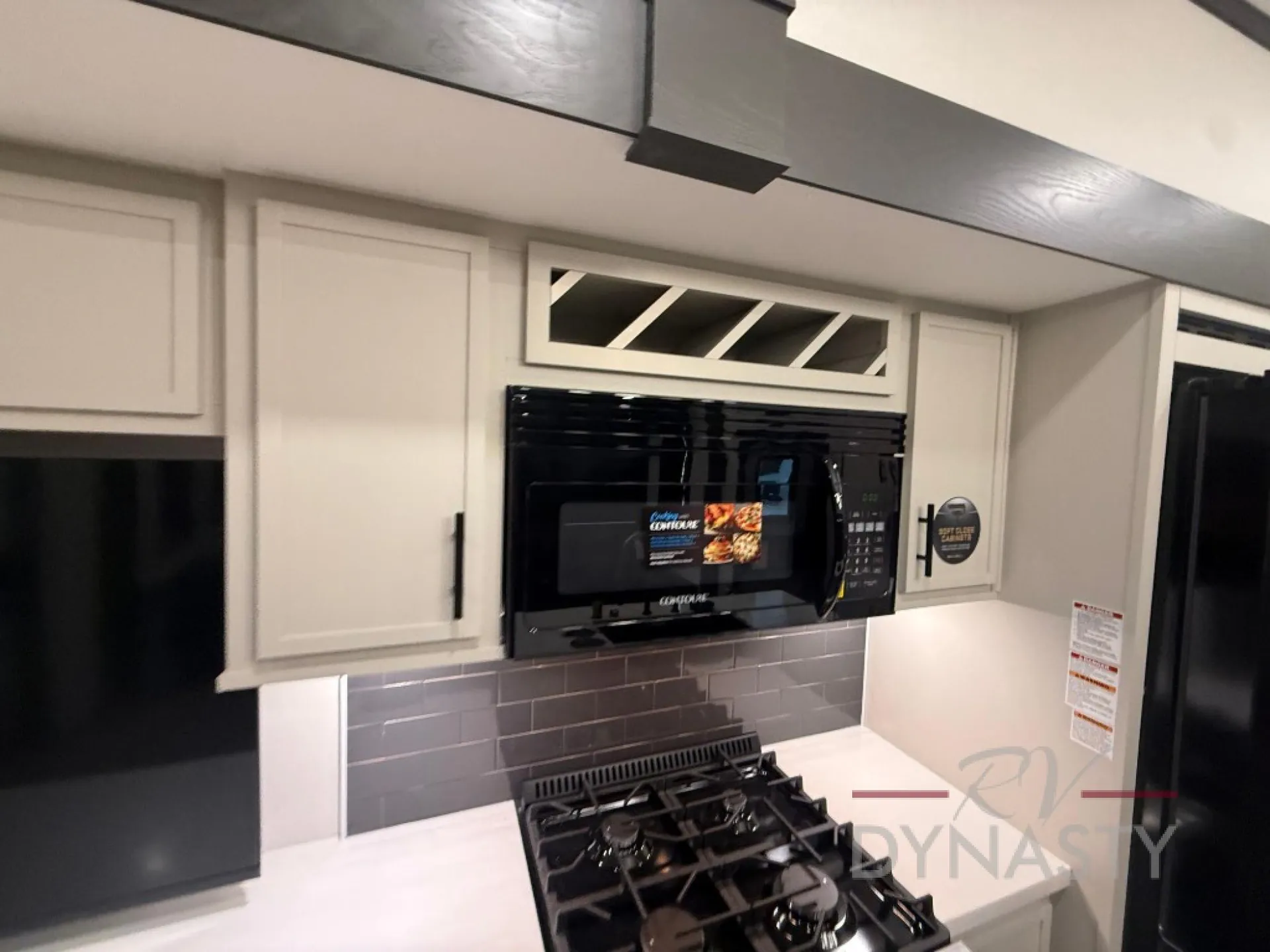 2027 Forest River Sanibel 40BUNK — Kitchen cooking area with gas cooktop, microwave, refrigerator edge, backsplash, counters, and overhead cabinets