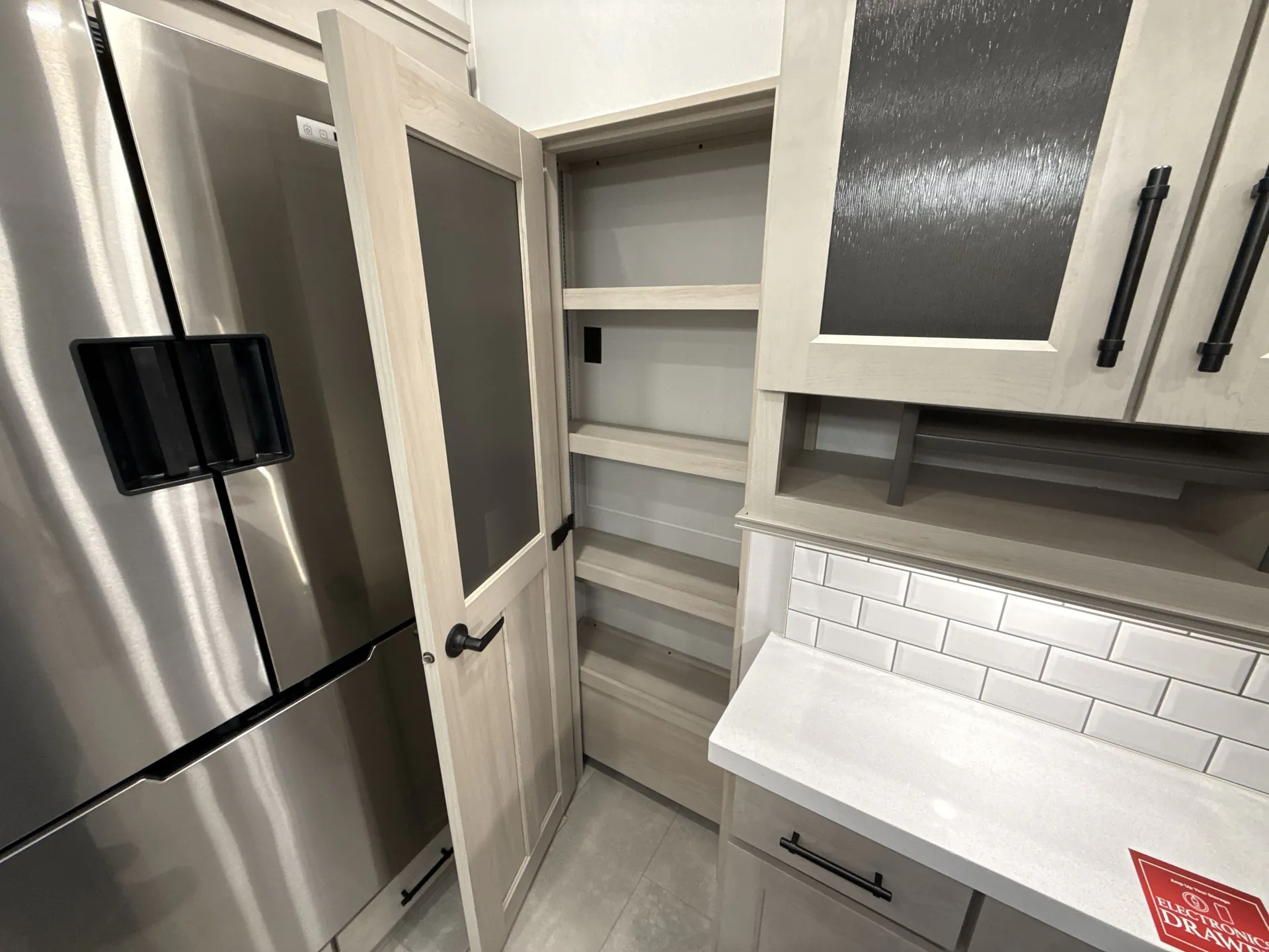 2026 Grand Design Solitude 391DL — Kitchen pantry shelves beside a stainless refrigerator, upper cabinets, backsplash, and countertop