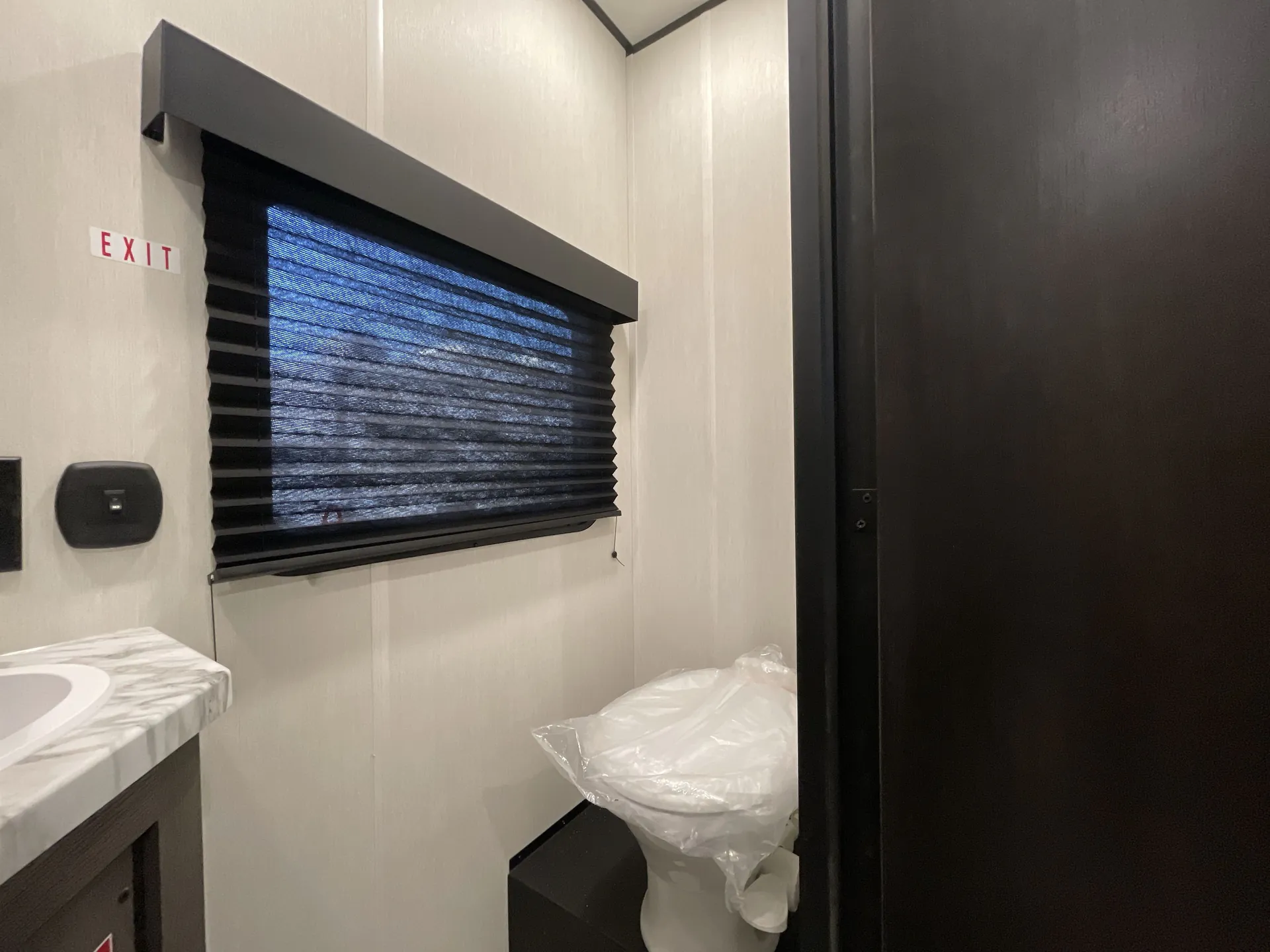 2026 Forest River Cherokee Wolf Pack 397STAY — Travel trailer bathroom with toilet, window shade, partial vanity countertop, and enclosed dark door