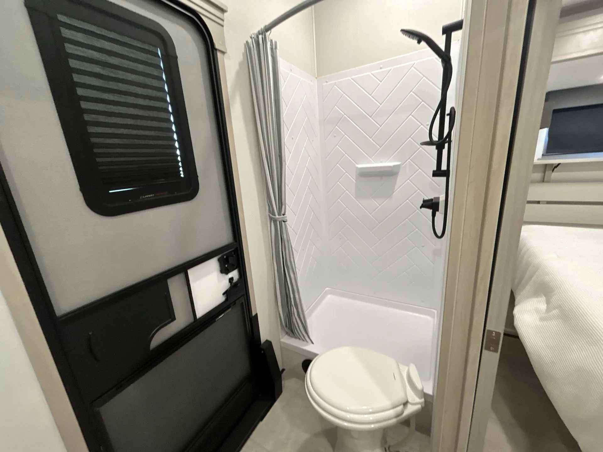 2026 Grand Design Solitude 391DL — Bathroom with toilet, corner shower, white tile surround, curtain, and black entry door beside the bedroom