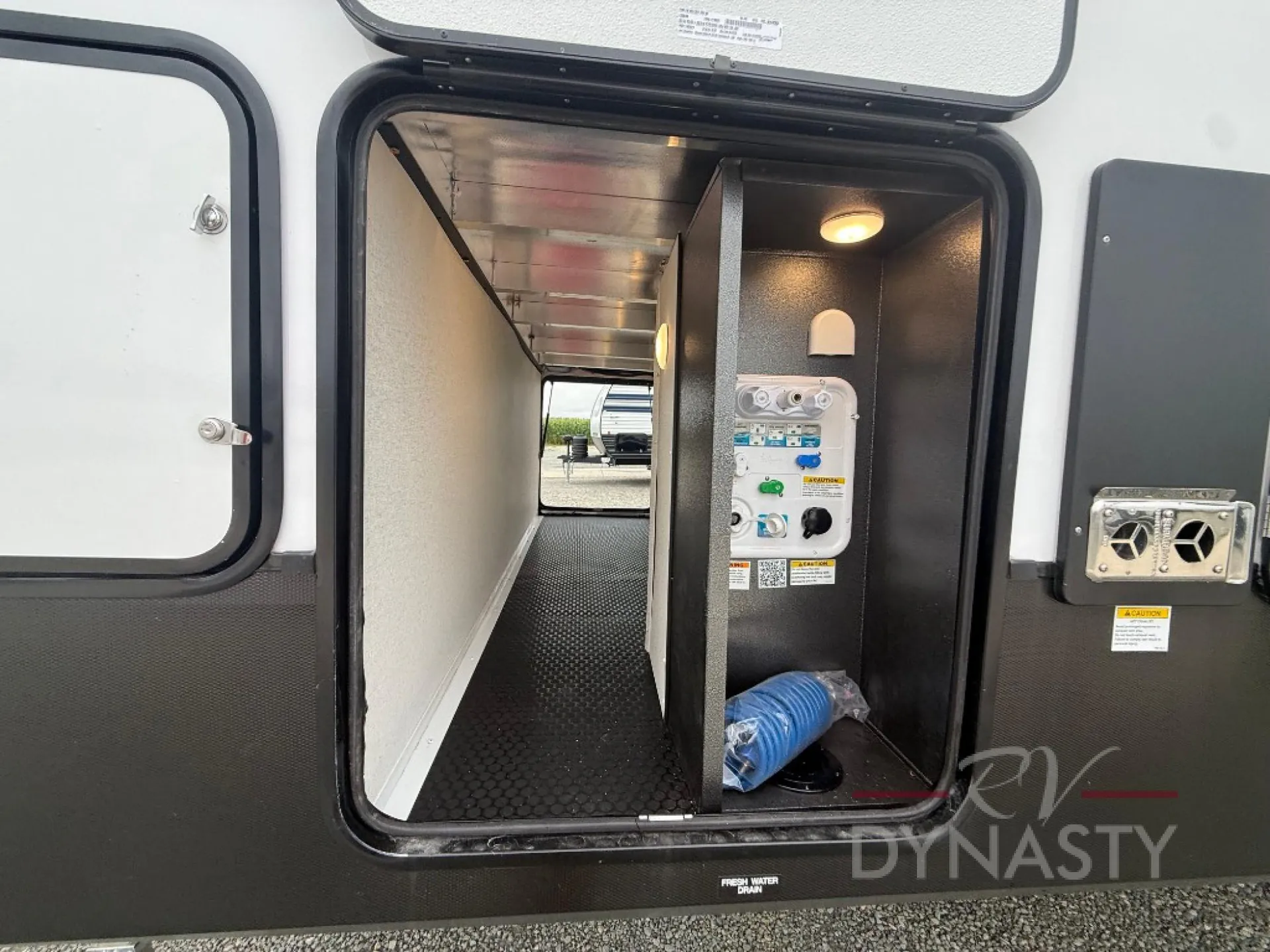 2027 Forest River Sanibel 40BUNK — Open exterior service compartment visibly contains labeled fresh-water plumbing and utility connections