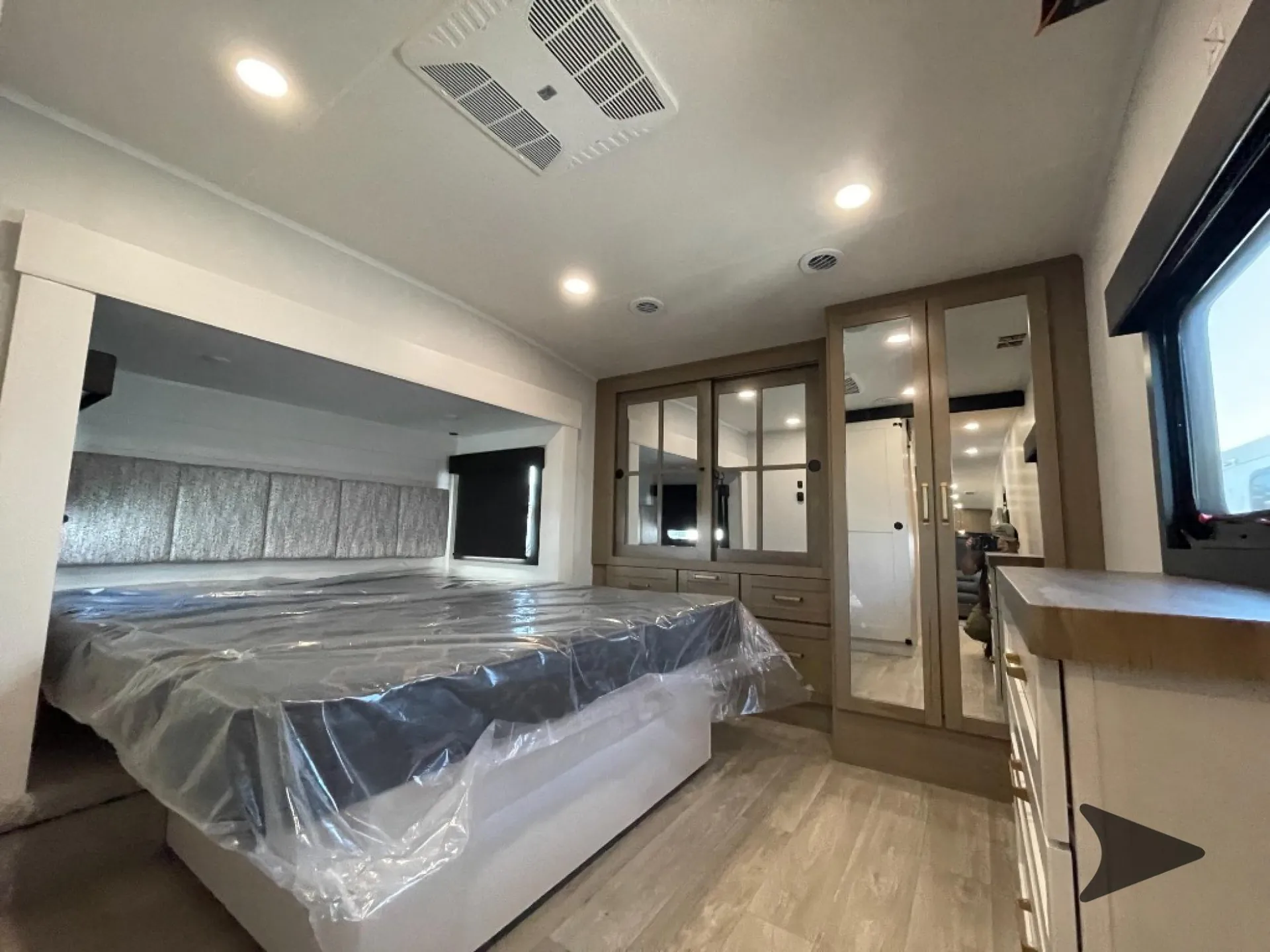 2027 Jayco Eagle 355MBQS — Main bedroom with a plastic-wrapped bed, mirrored wardrobe, dresser cabinetry, windows, and ceiling ventilation