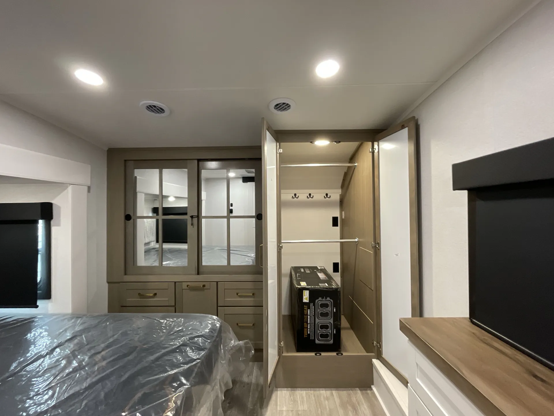 2027 Jayco Eagle 355MBQS — Bedroom showing a plastic-covered bed, mirrored wardrobe, open closet, dresser, and wall-mounted television