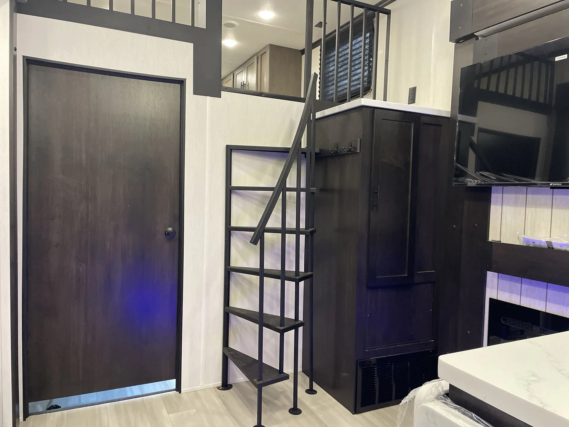 2026 Forest River Cherokee Wolf Pack 397STAY — Travel trailer ladder leads to an elevated loft beside tall cabinetry, a window, television, and dark entry door