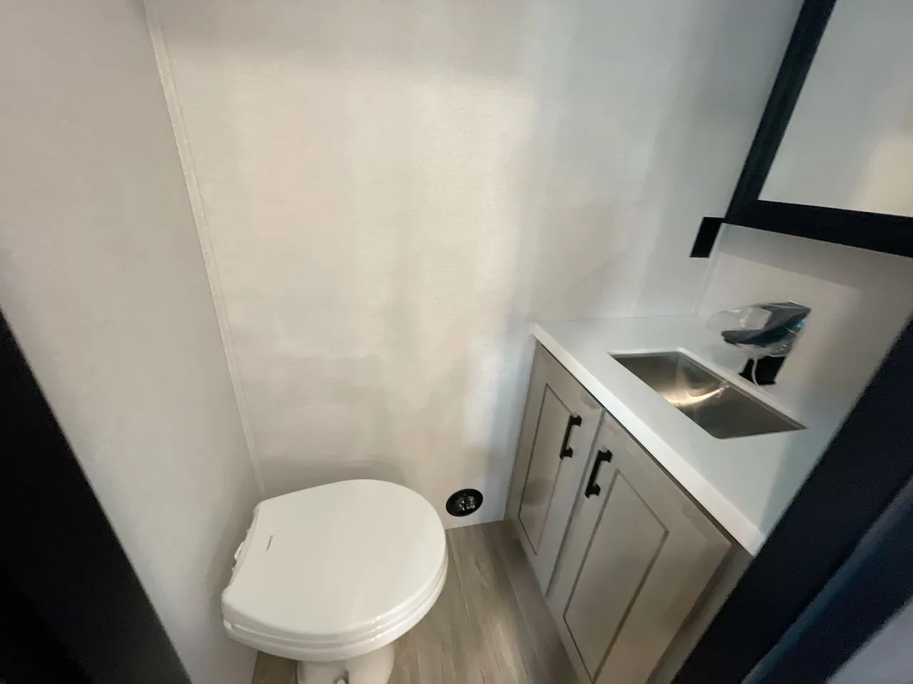 2027 Jayco Pinnacle 39FLOK — Compact bathroom with a toilet, stainless sink, white vanity countertop, and lower cabinets