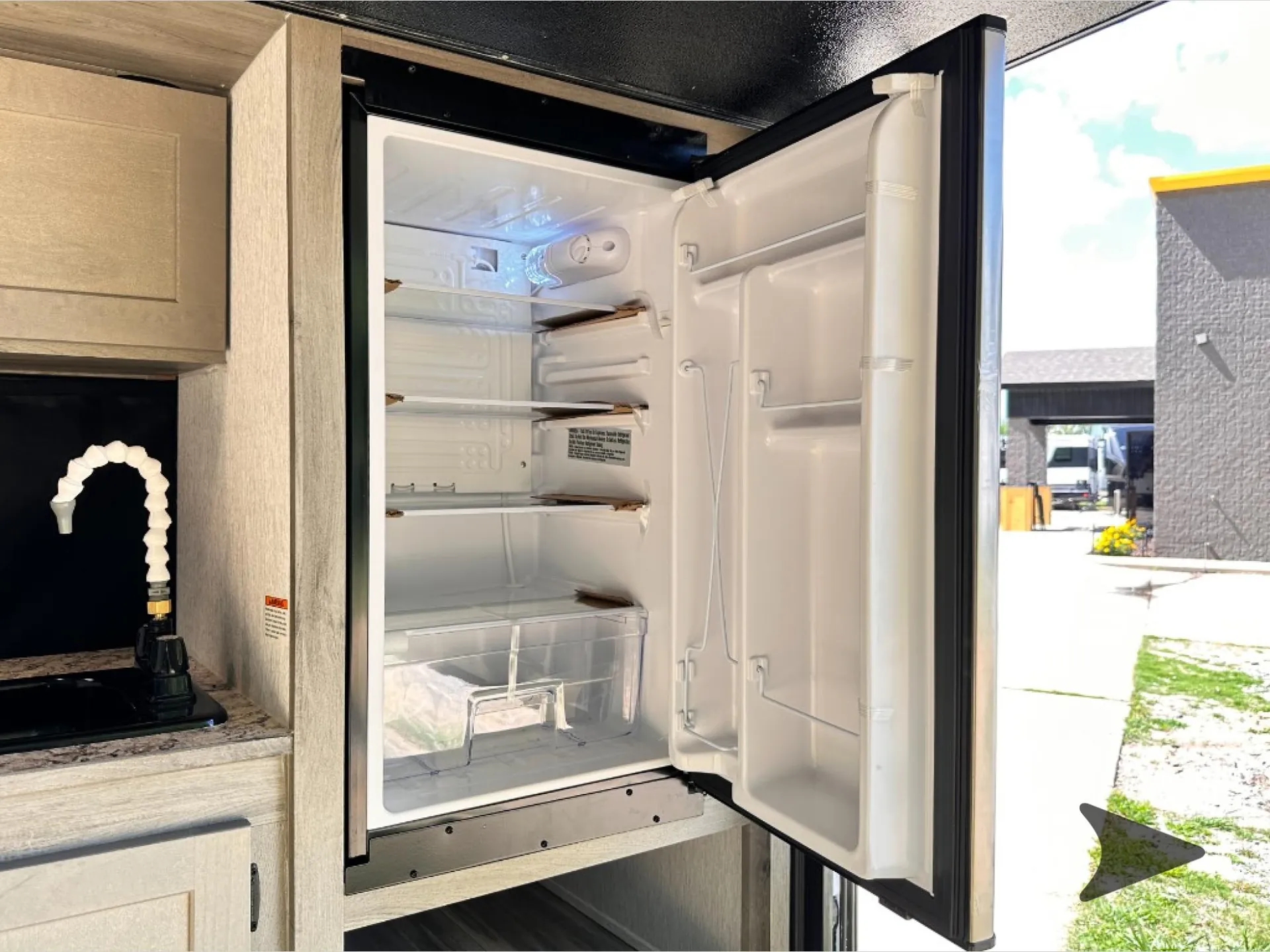 2026 Wayfinder GO LITE LTD Solo — Open compact refrigerator with empty shelves and door bins beside the camper kitchen counter