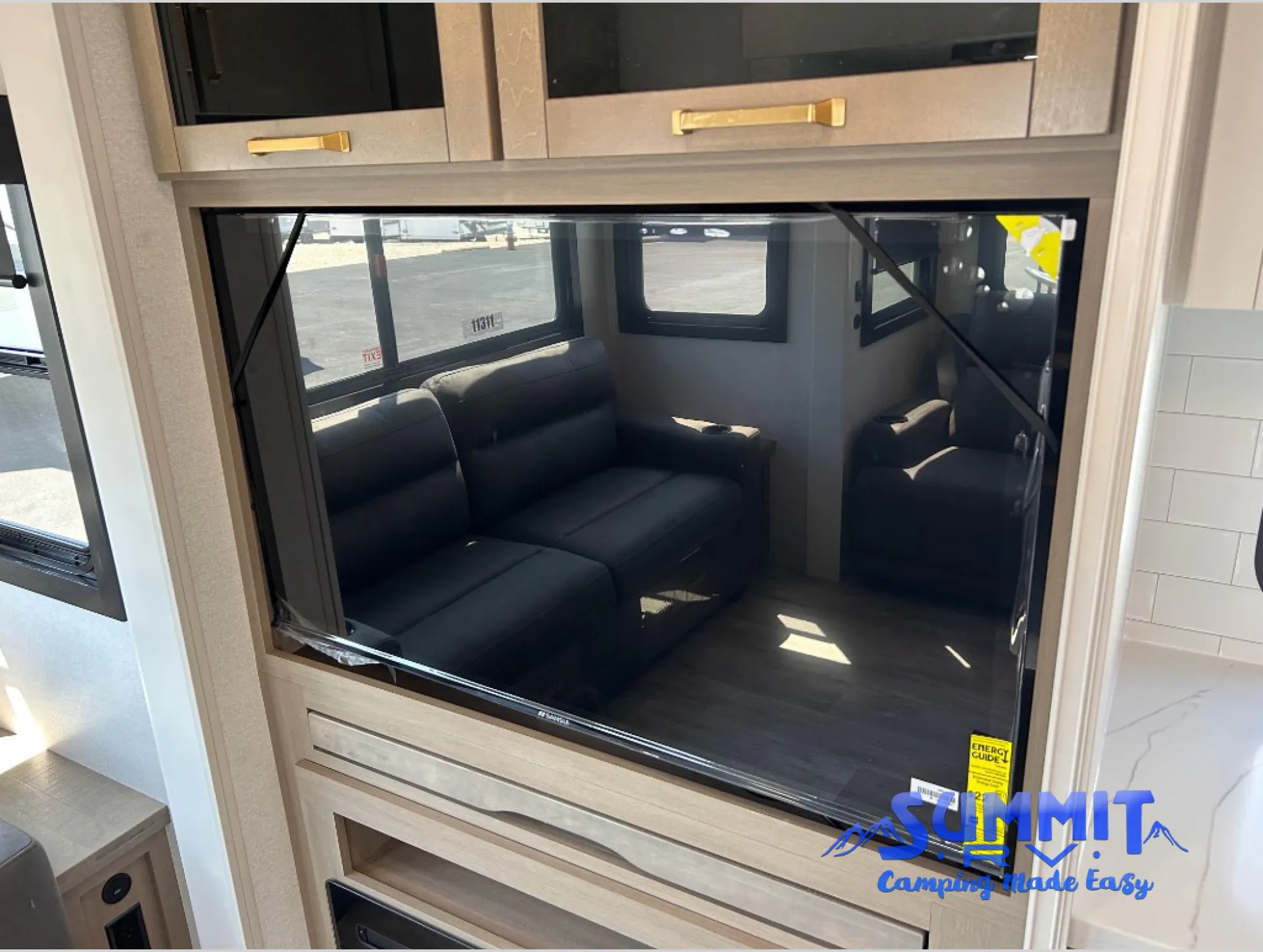 2027 Jayco Eagle 355MBQS — Living area with two dark sofas visible through a large entertainment-center television opening and surrounding cabinetry