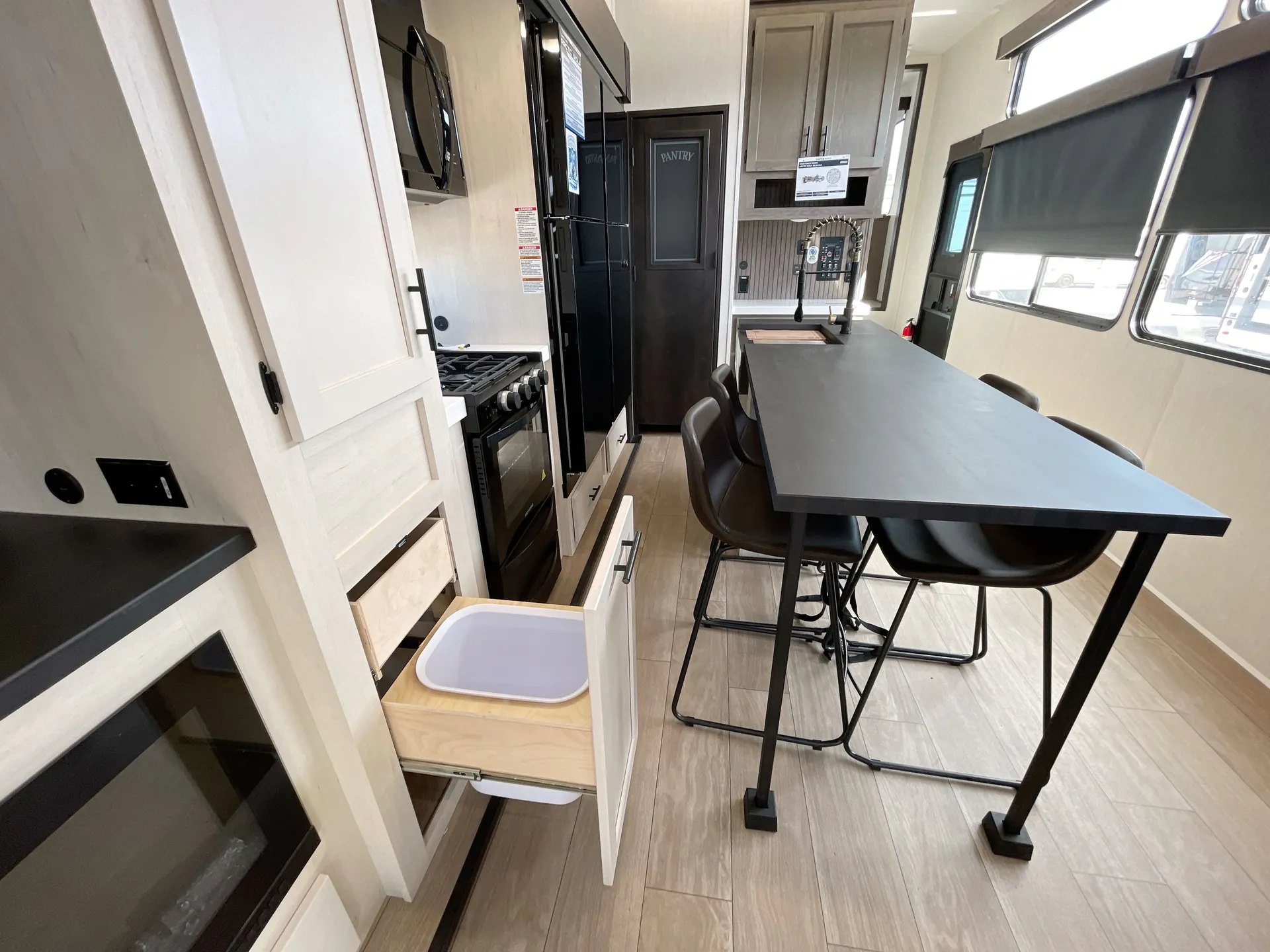 2026 Forest River Arctic Wolf 38LEAH.G — Fifth wheel dining table with four chairs beside the kitchen range, refrigerator, sink, cabinetry, and open drawers