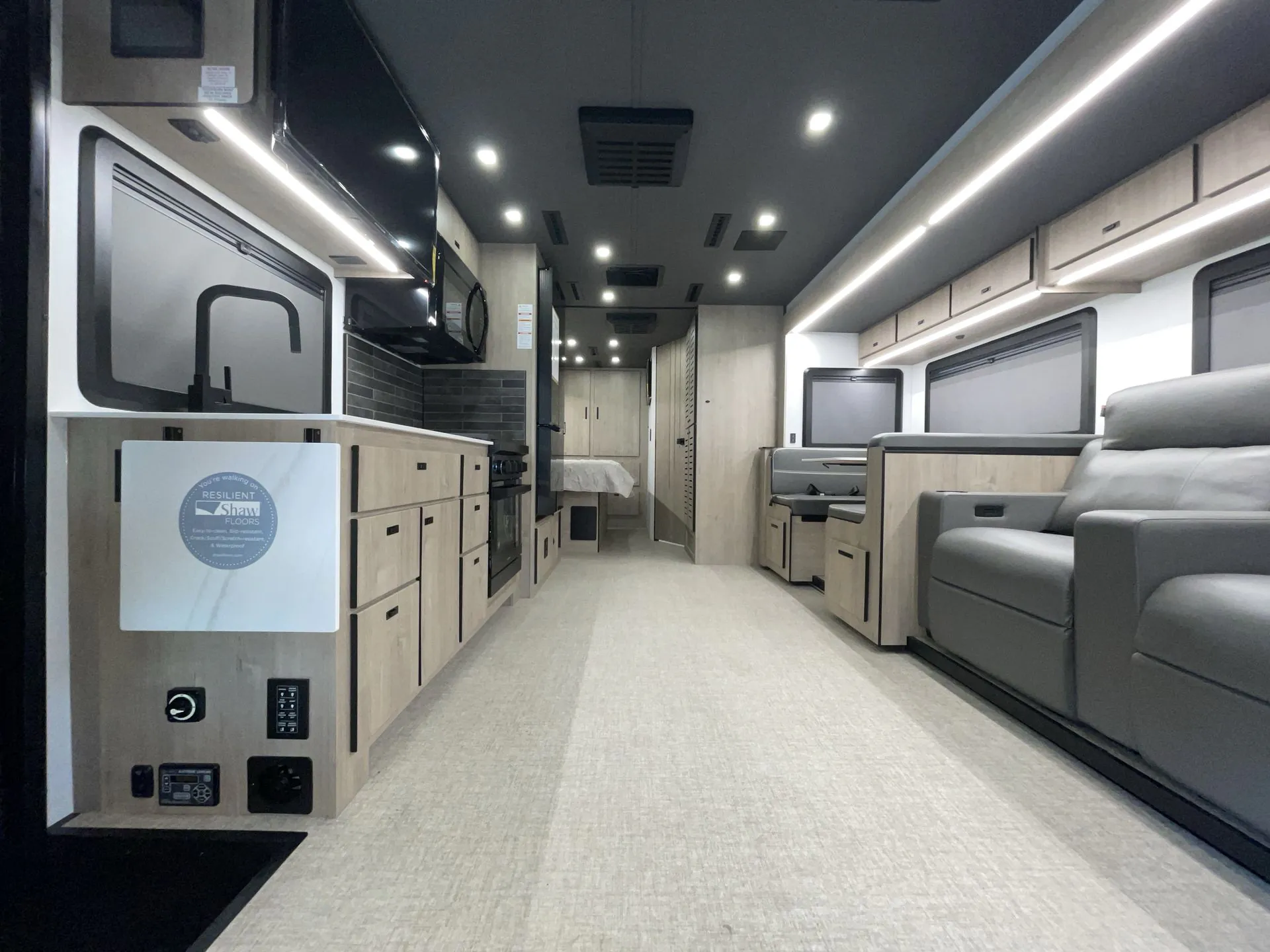 2027 Grand Design Lineage Series F 31ZW — Class C motorhome kitchen with sink, cooktop, refrigerator, lounge recliners, and a bedroom visible down the aisle