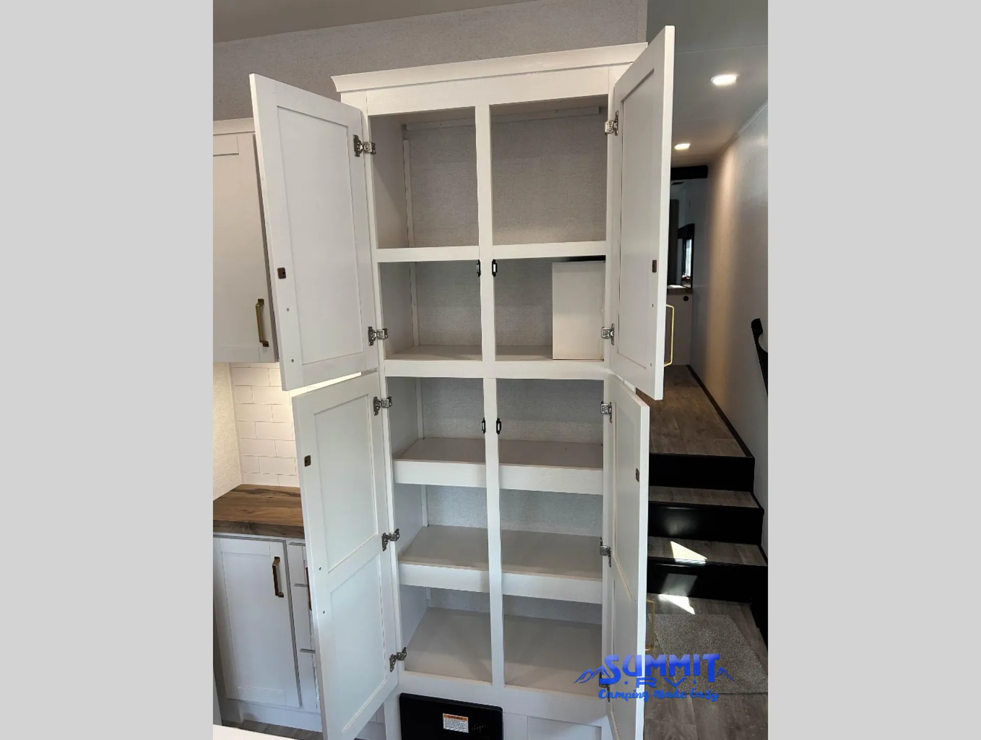 2027 Jayco Eagle 355MBQS — Tall open storage cabinet with multiple shelves beside kitchen cabinetry, countertop, and stairs