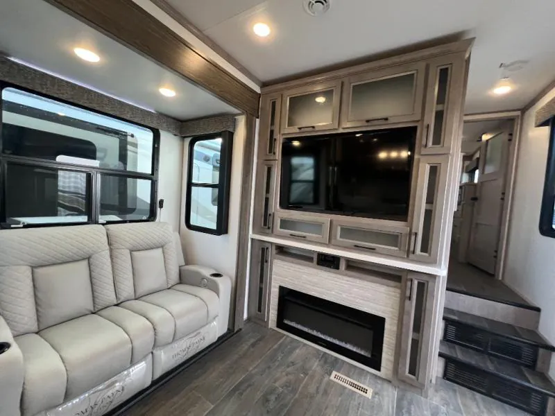 2023 Dutchmen Voltage 4225 — Living-room entertainment center with television, fireplace, storage cabinets, and a recliner beside it