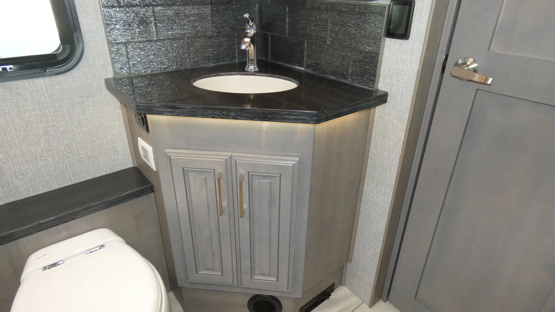 2026 Fleetwood Discovery LXE 40G — Bathroom vanity with oval sink, black countertop, gray cabinet, toilet, and adjacent door