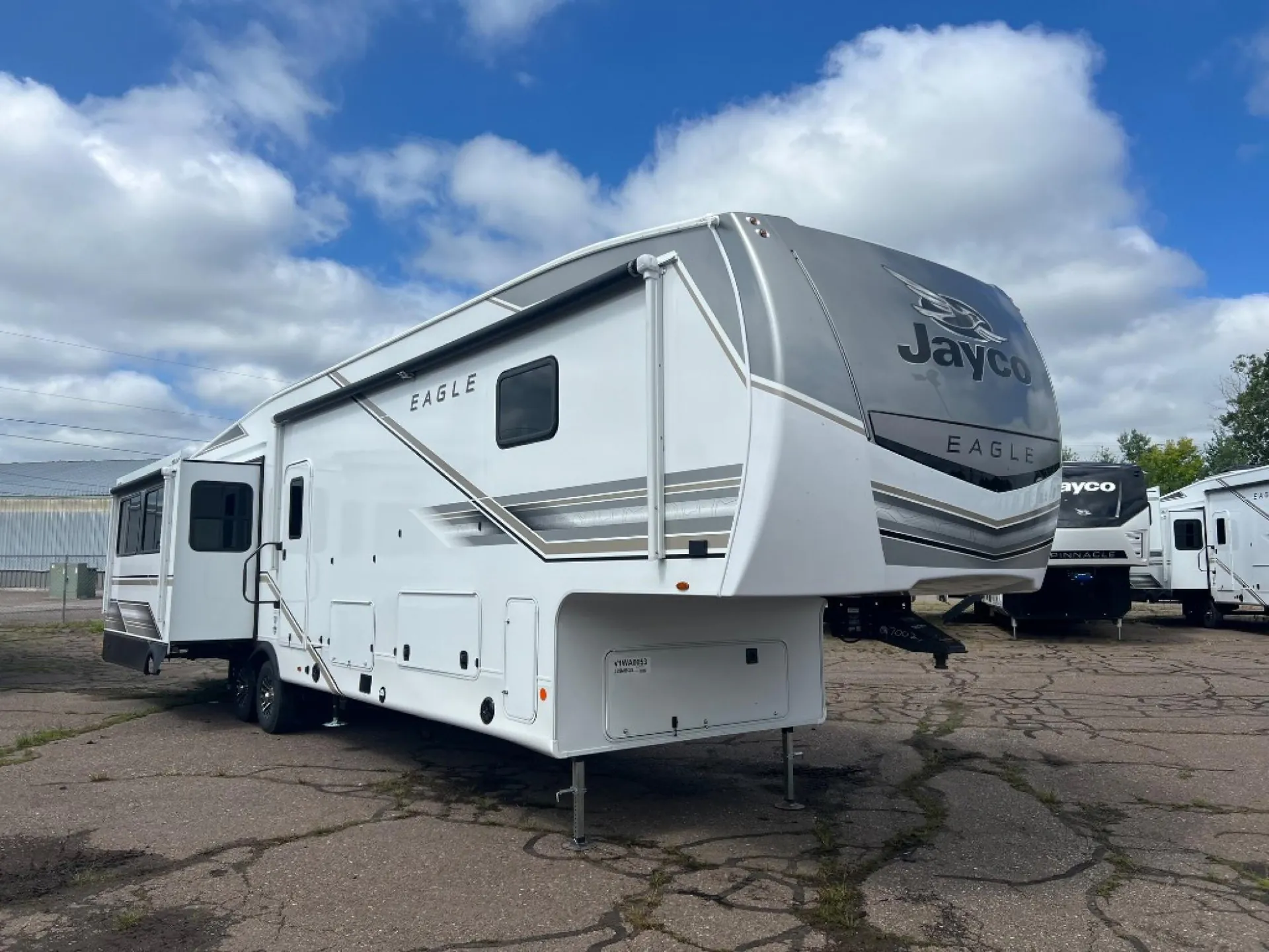 2027 Jayco Eagle 355MBQS — The outside of a Jayco Eagle fifth-wheel RV, including its front cap, side wall, slide-out, hitch area, wheels, and exterior storage doors