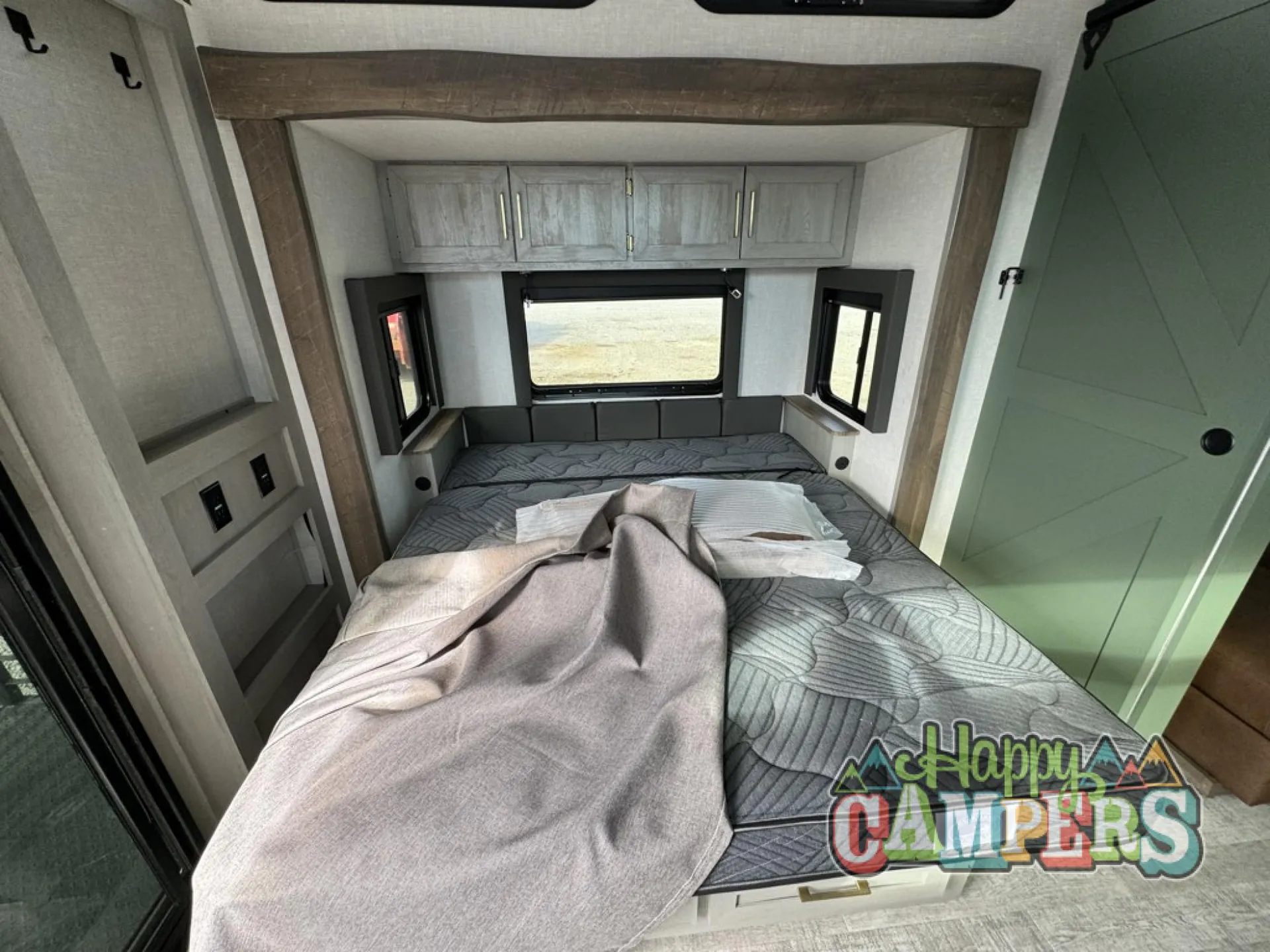 2025 Forest River IBEX RVS3 — Main bedroom with a large bed, overhead storage cabinets, windows, and a closed interior door