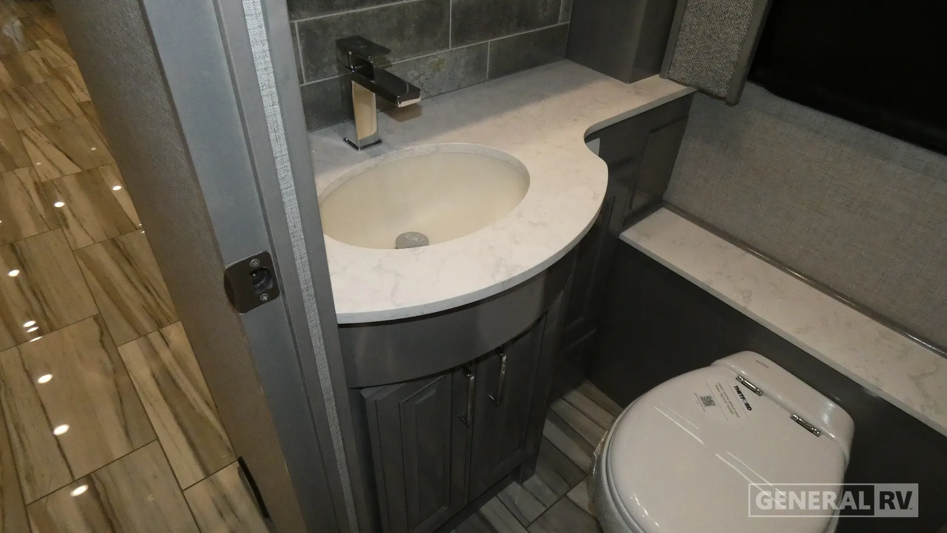 2026 American Coach American Dream 45A — Bathroom vanity sink and faucet beside a covered toilet, cabinet storage, and tiled floor