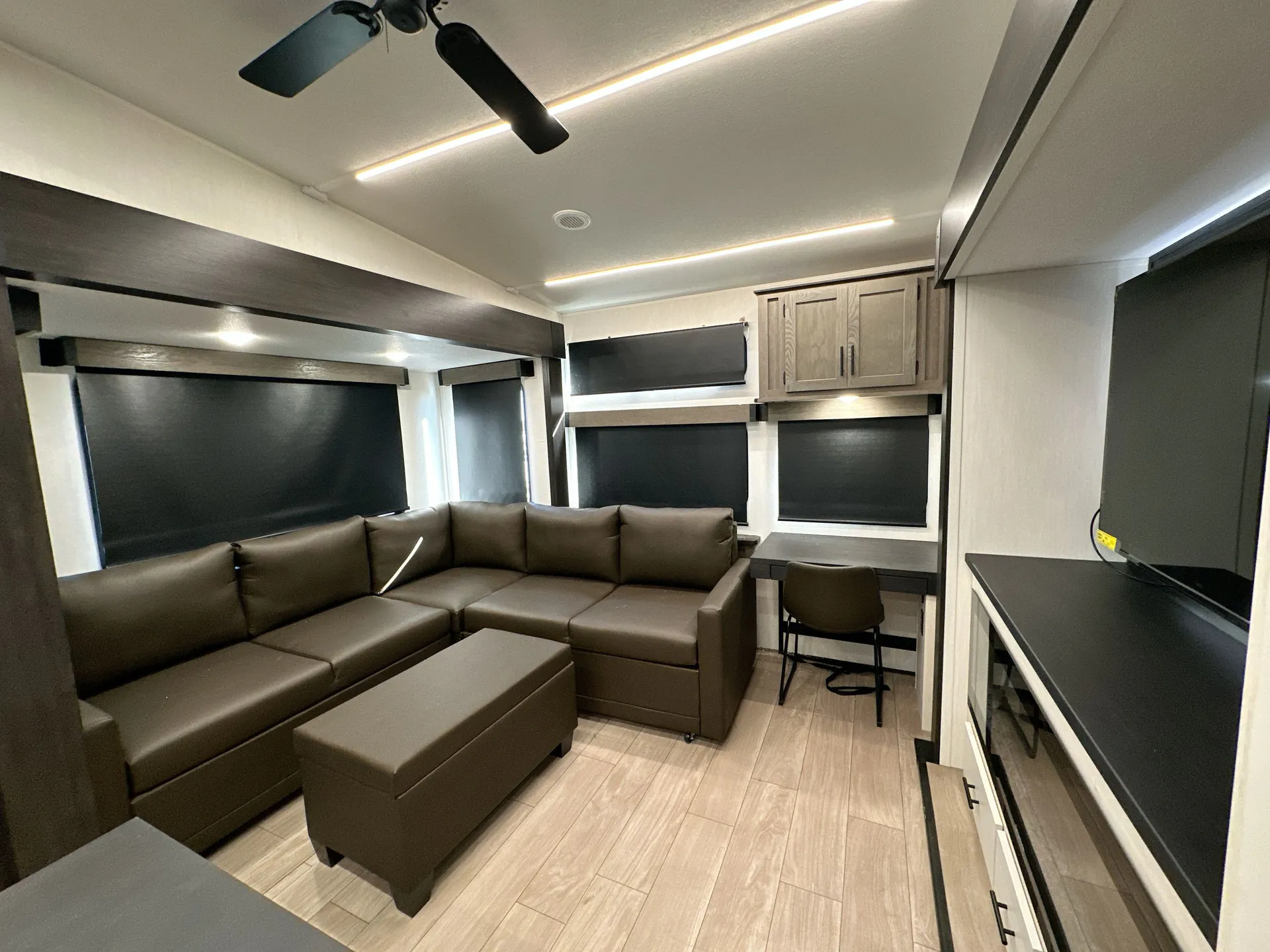 2026 Forest River Arctic Wolf 38LEAH.G — Fifth wheel lounge with large sectional sofa, ottoman, windows with roller shades, desk, and entertainment cabinetry