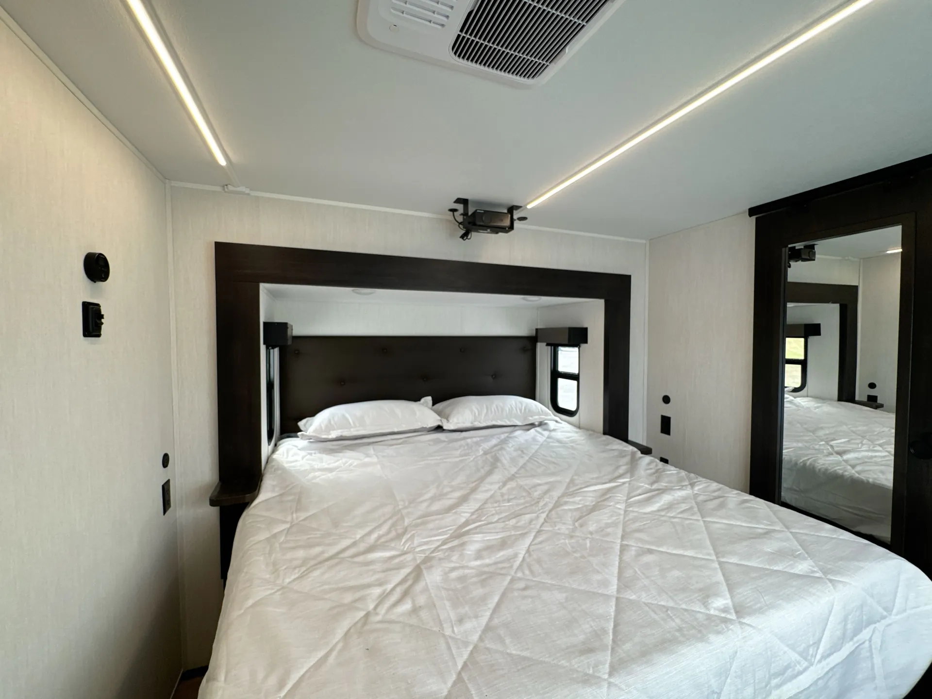 2026 Forest River Arctic Wolf 38LEAH.G — Main bedroom with a large bed, padded headboard, bedside windows, and mirrored wardrobe door