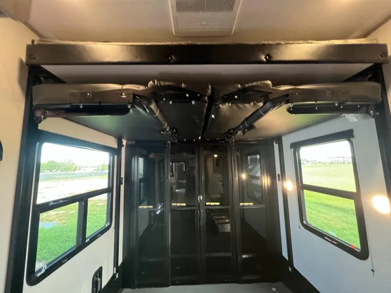 2023 Dutchmen Voltage 4225 — Toy-hauler garage showing a broad open cargo floor, black fold-away structures, windows, and rear loading space