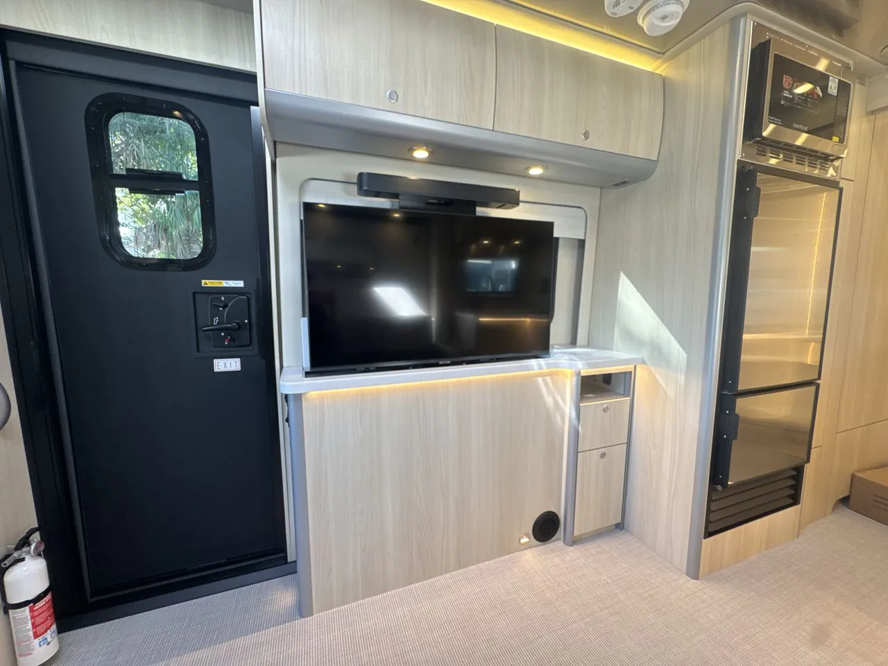 2026 Airstream Atlas Murphy Suite — Van entertainment wall with television, soundbar, storage cabinetry, entry door, and adjacent refrigerator