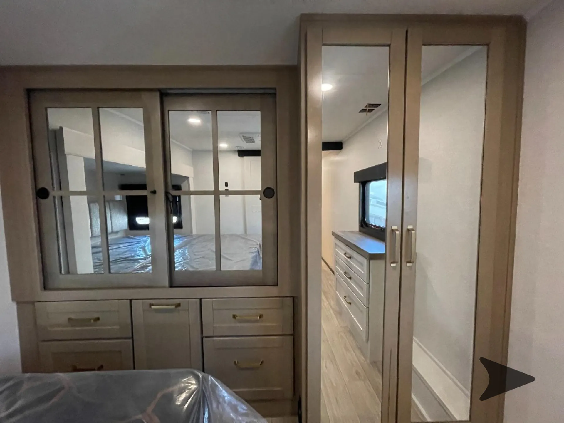 2027 Jayco Eagle 355MBQS — Fifth-wheel bedroom with mirrored wardrobe, dresser drawers, bed edge, and adjoining closet doorway