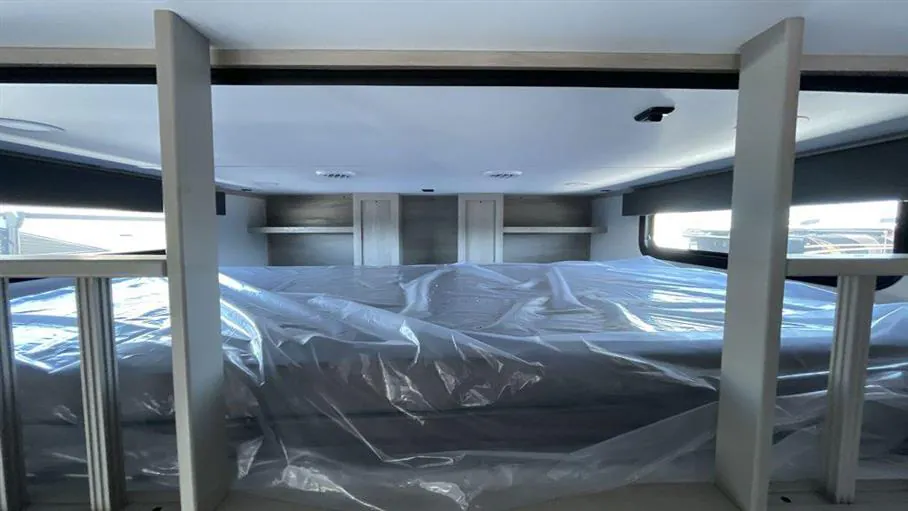 2026 Grand Design Solitude 391DL — Elevated fifth wheel loft sleeping platform with mattress, side rails, overhead cabinets, and windows