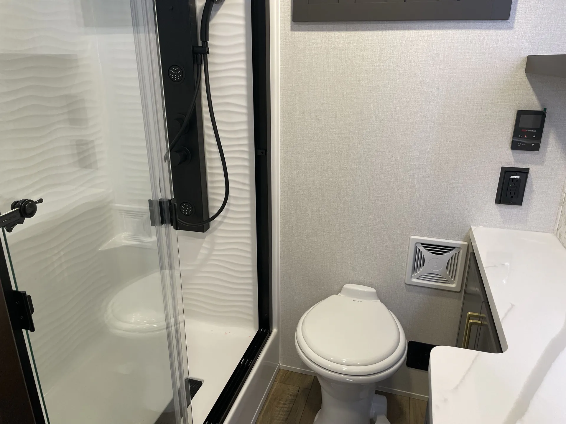 2026 Forest River Cedar Creek Cottage 41FWC — Bathroom view showing glass shower enclosure, shower fixtures, toilet, vanity edge, controls, and ventilation grille