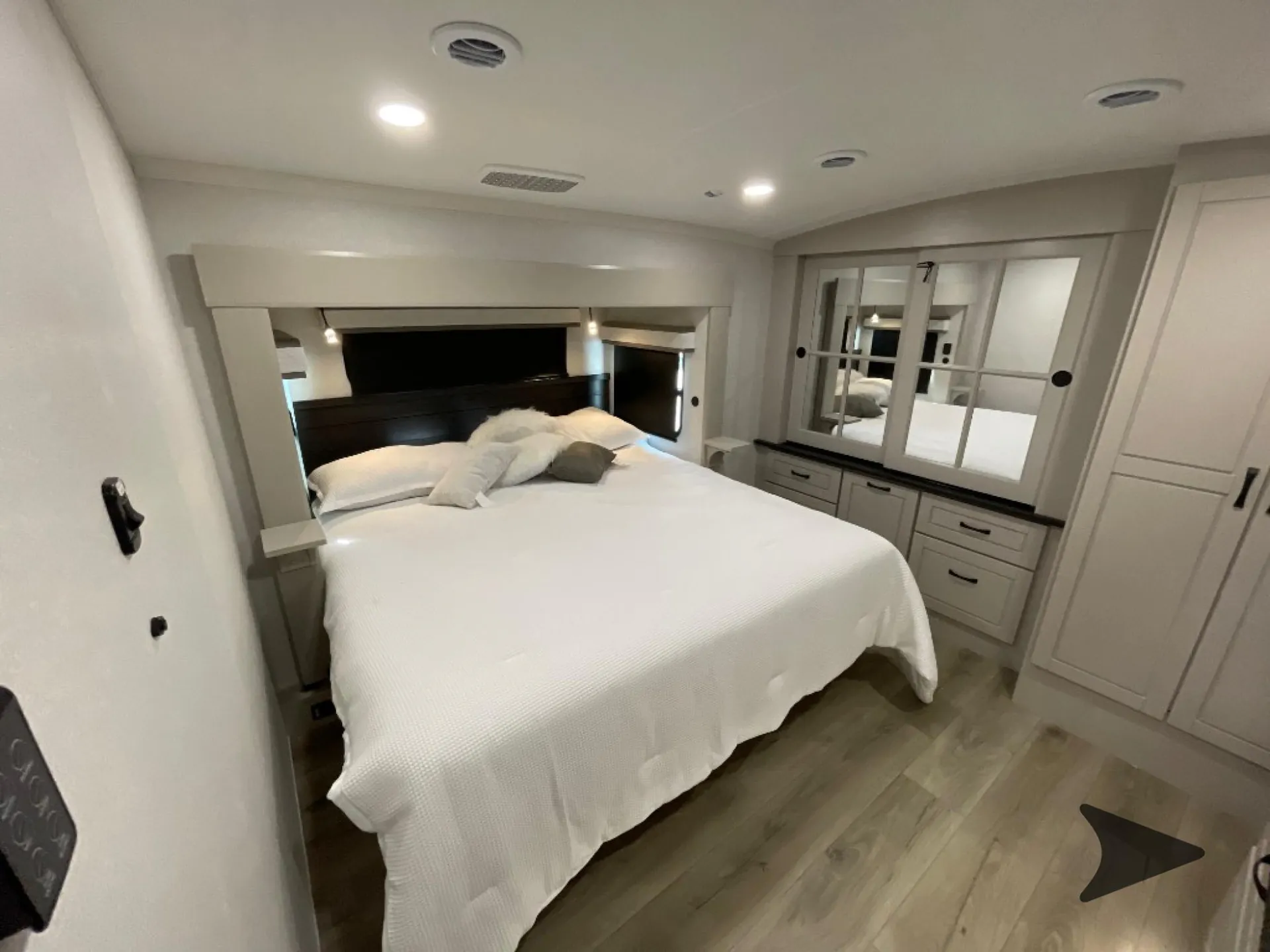 2026 Jayco North Point 377RLBH — Main bedroom with a made bed, mirrored dresser, drawers, and a tall wardrobe cabinet