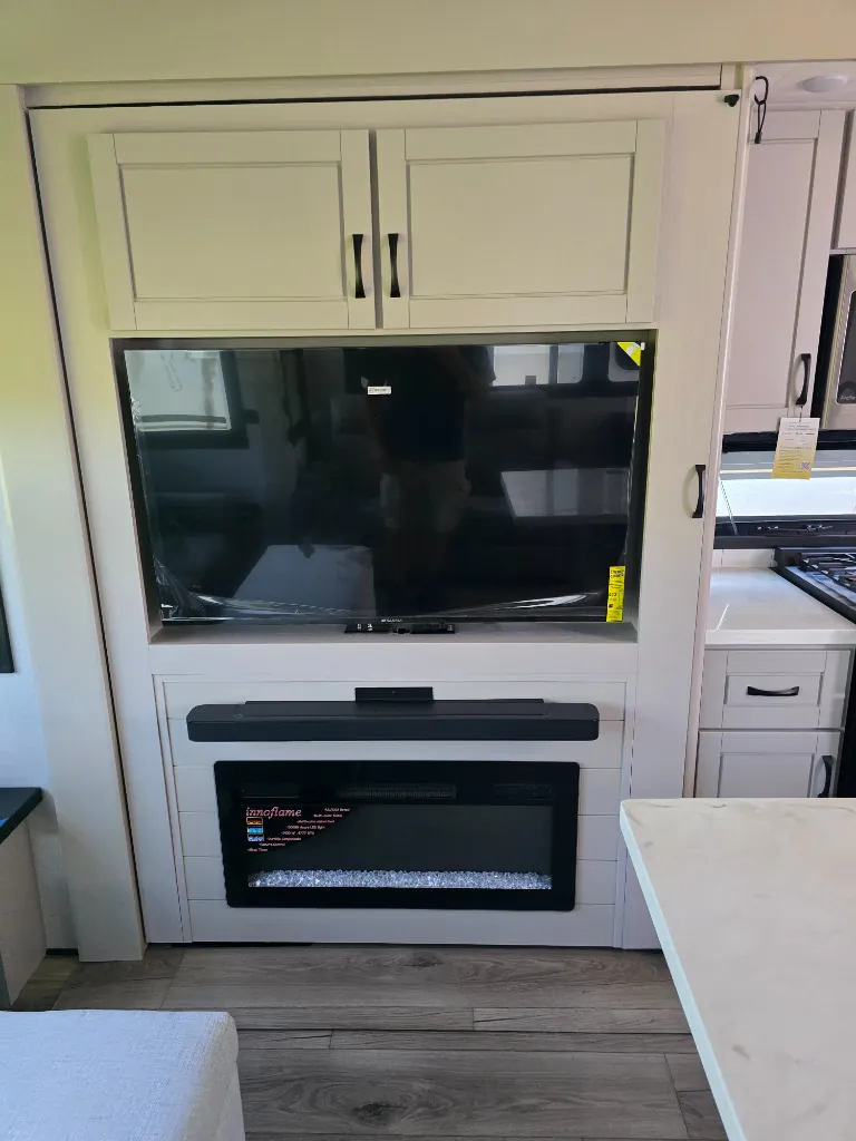 2026 Jayco North Point 377RLBH — Living entertainment wall with television, soundbar, electric fireplace, and adjacent kitchen range and cabinetry