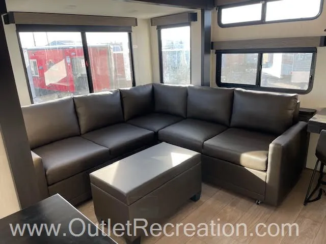 2026 Forest River Arctic Wolf 38LEAH.G — L-shaped leather sofa surrounding a rectangular ottoman beneath multiple RV windows