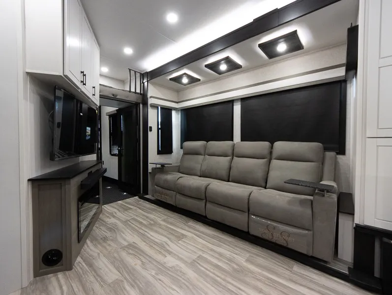2025 Jayco Seismic Luxury Series 4113 — Fifth wheel living area with a reclining sofa, television, dark window shades, and overhead lighting