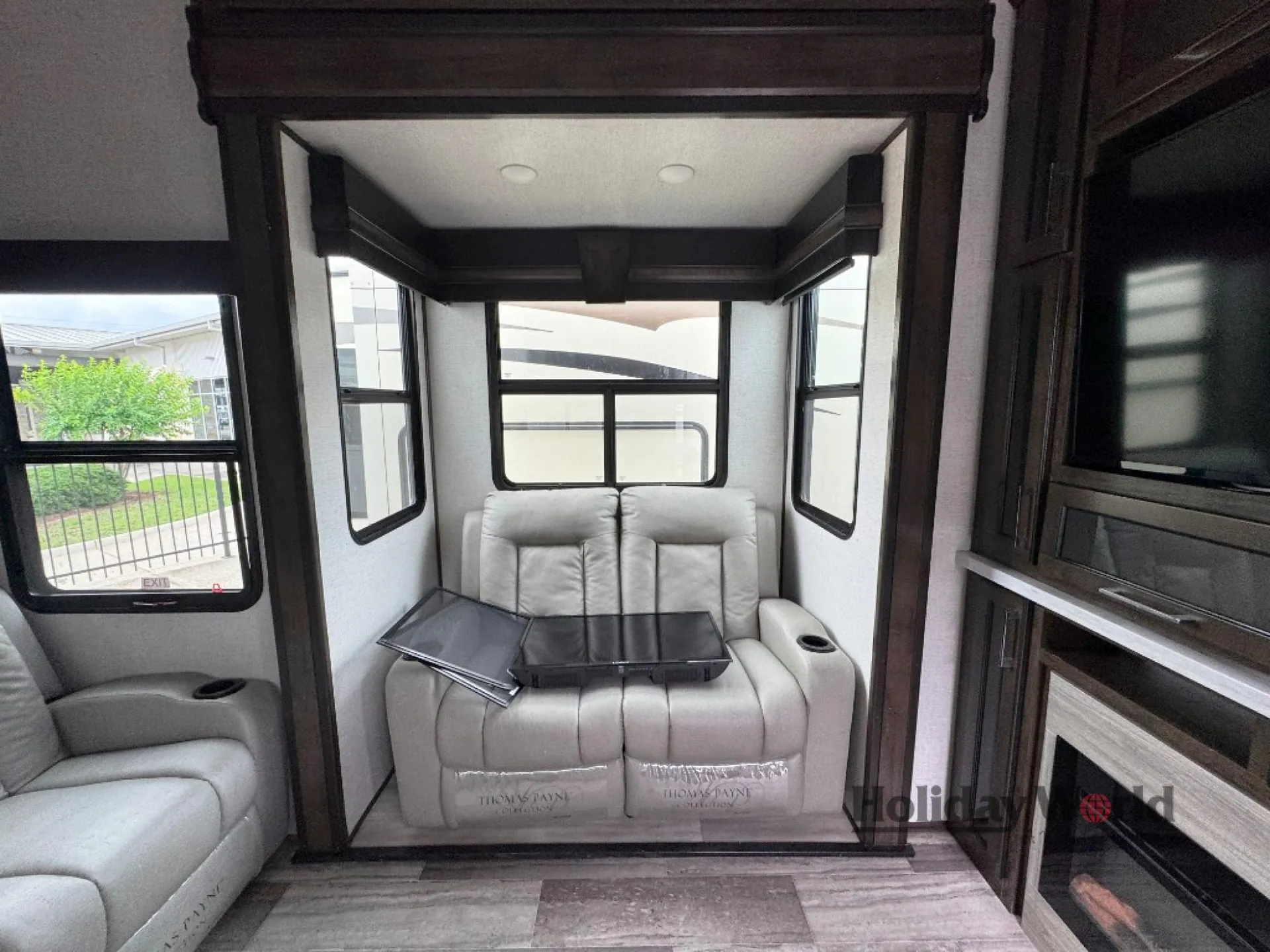 2022 Dutchmen Voltage 4225 — Living area with reclining theater seating, folding table, panoramic windows, and entertainment fireplace wall