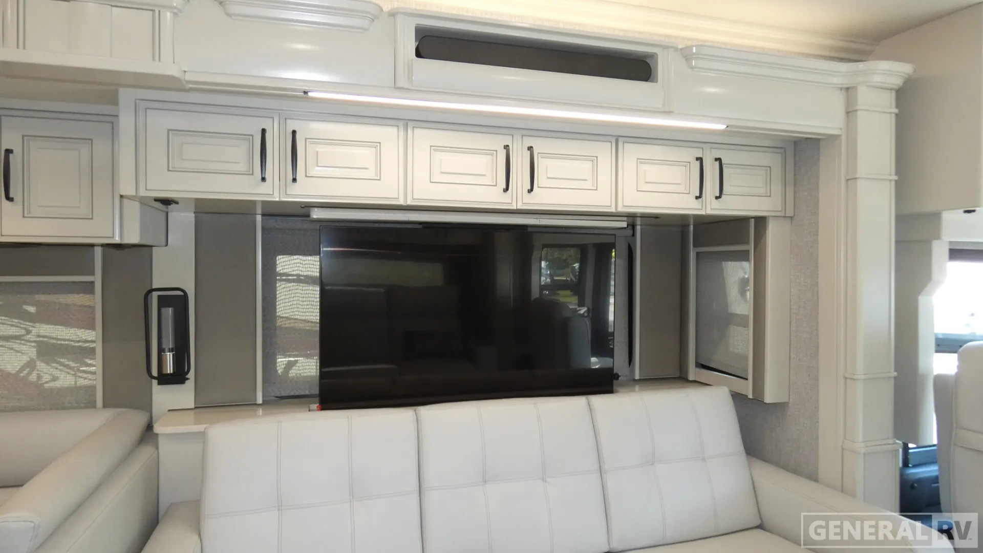 2026 American Coach American Dream 45A — White living-room sofa beneath a large television, overhead cabinets, window shades, and side storage