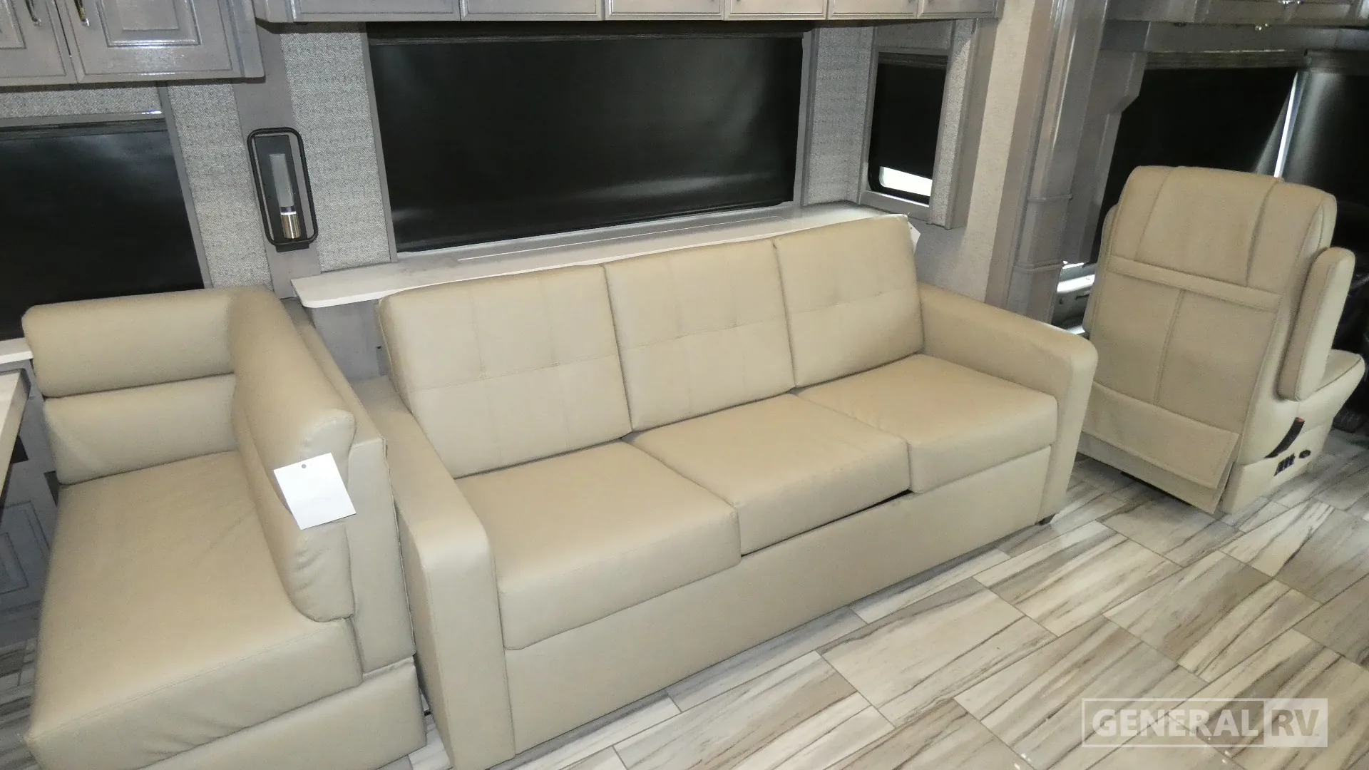 2026 American Coach American Dream 45A — Living area with a cream sofa, matching recliner, overhead television, windows, and wood-look flooring