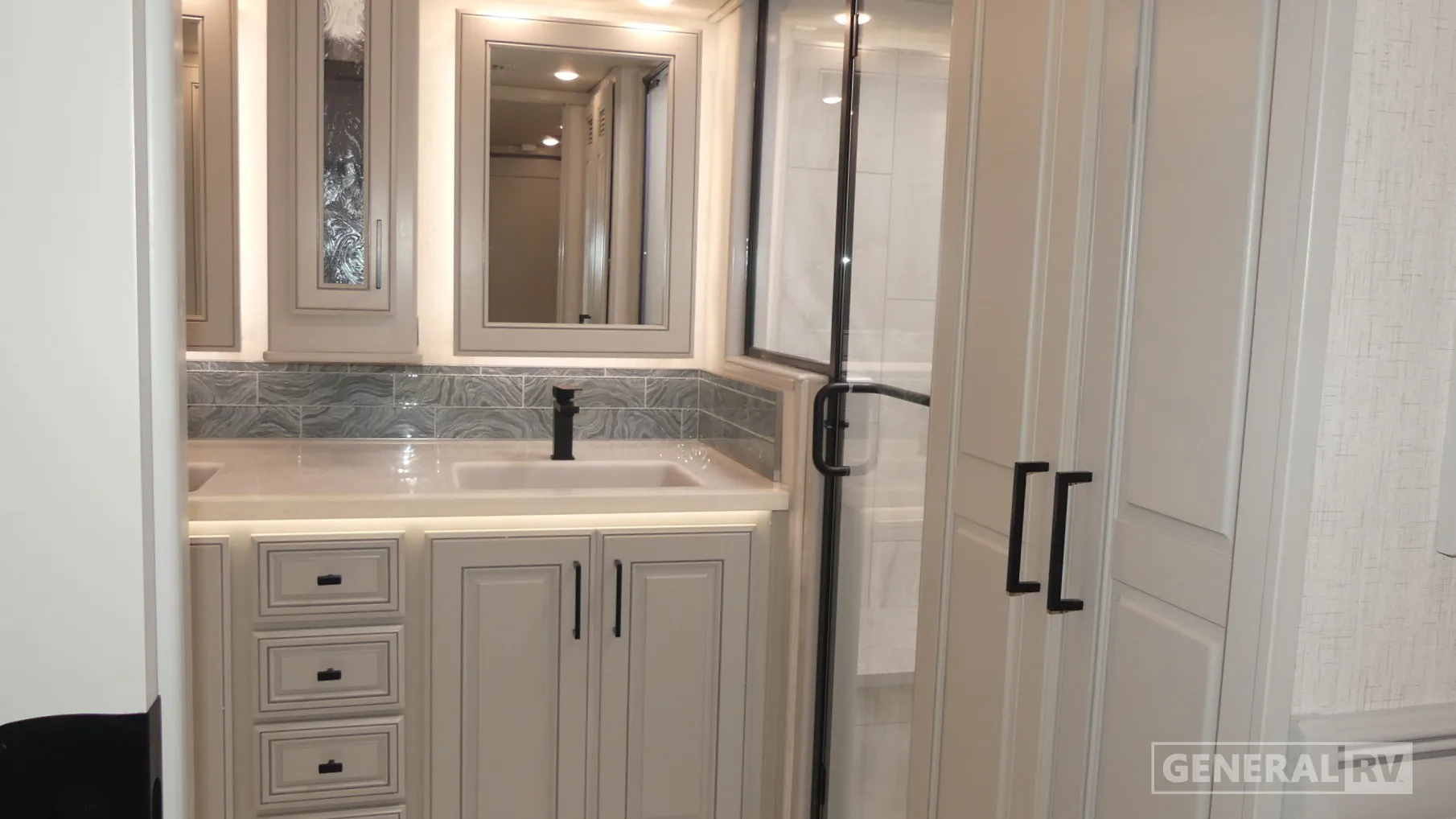 2027 Fleetwood Discovery LXE 40M — Bathroom vanity with double mirrors, sink, drawers, cabinets, and adjacent glass shower enclosure