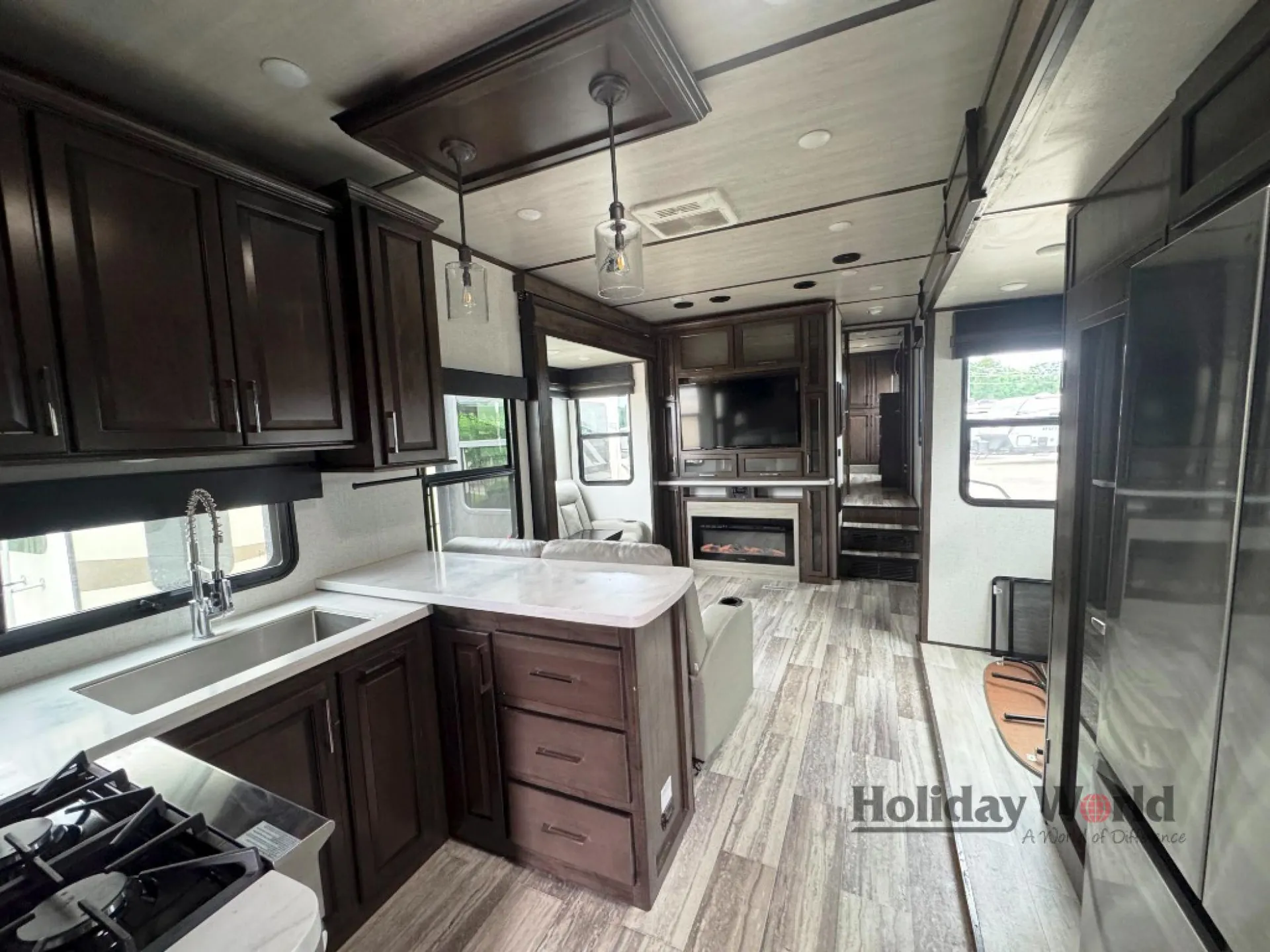 2022 Dutchmen Voltage 4225 — Kitchen island with sink and cabinetry overlooking recliners, entertainment center, fireplace, and refrigerator