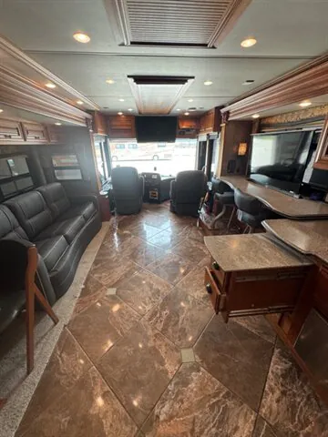 2016 Newmar Dutch Star 4369 — Motorhome lounge with sofa, front captain chairs, entertainment television, and kitchen counter cabinetry