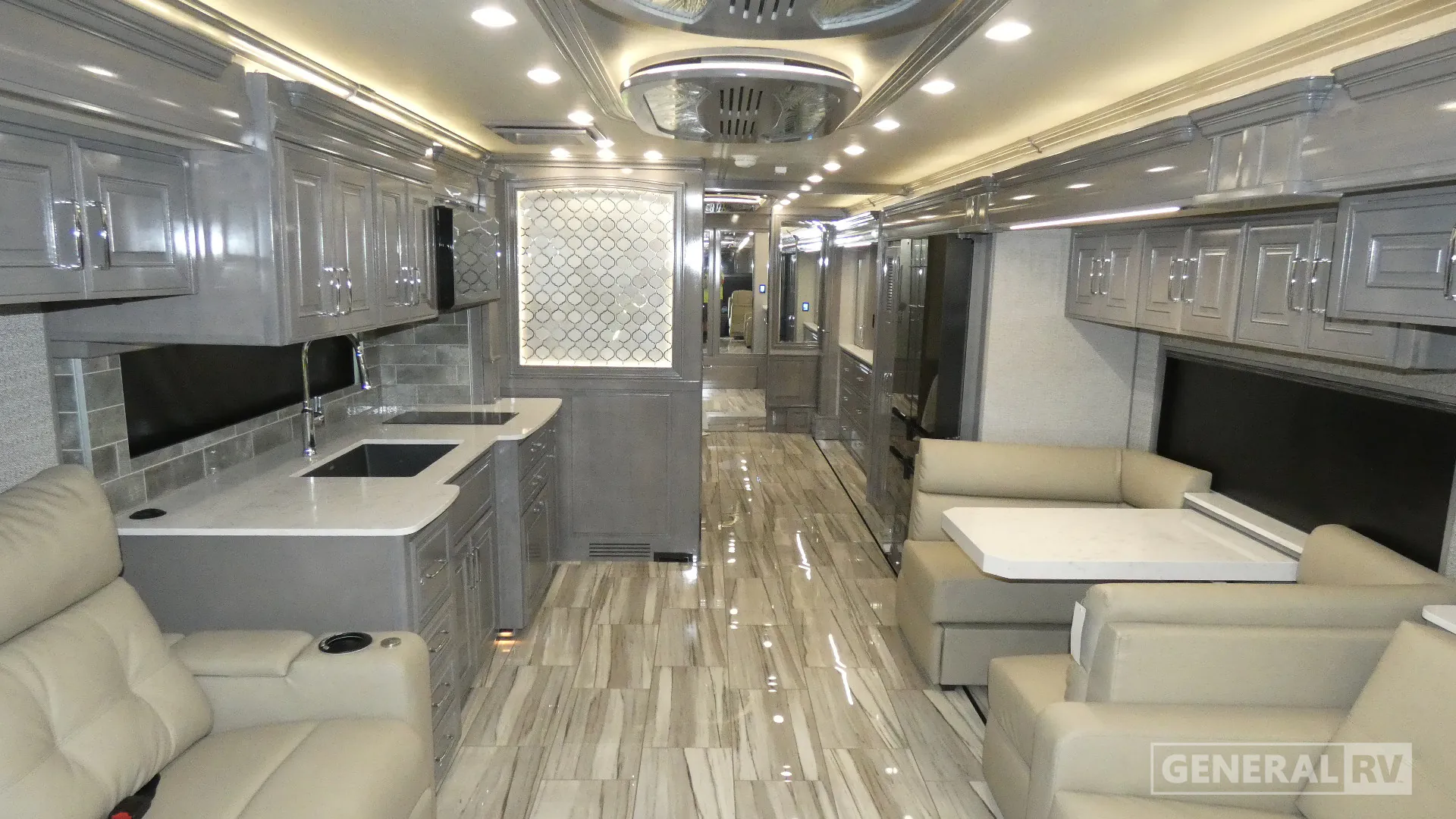2026 American Coach American Dream 45A — Class A kitchen with dual sinks, cooktop, extensive cabinetry, adjacent lounge seating, and a dinette along the aisle