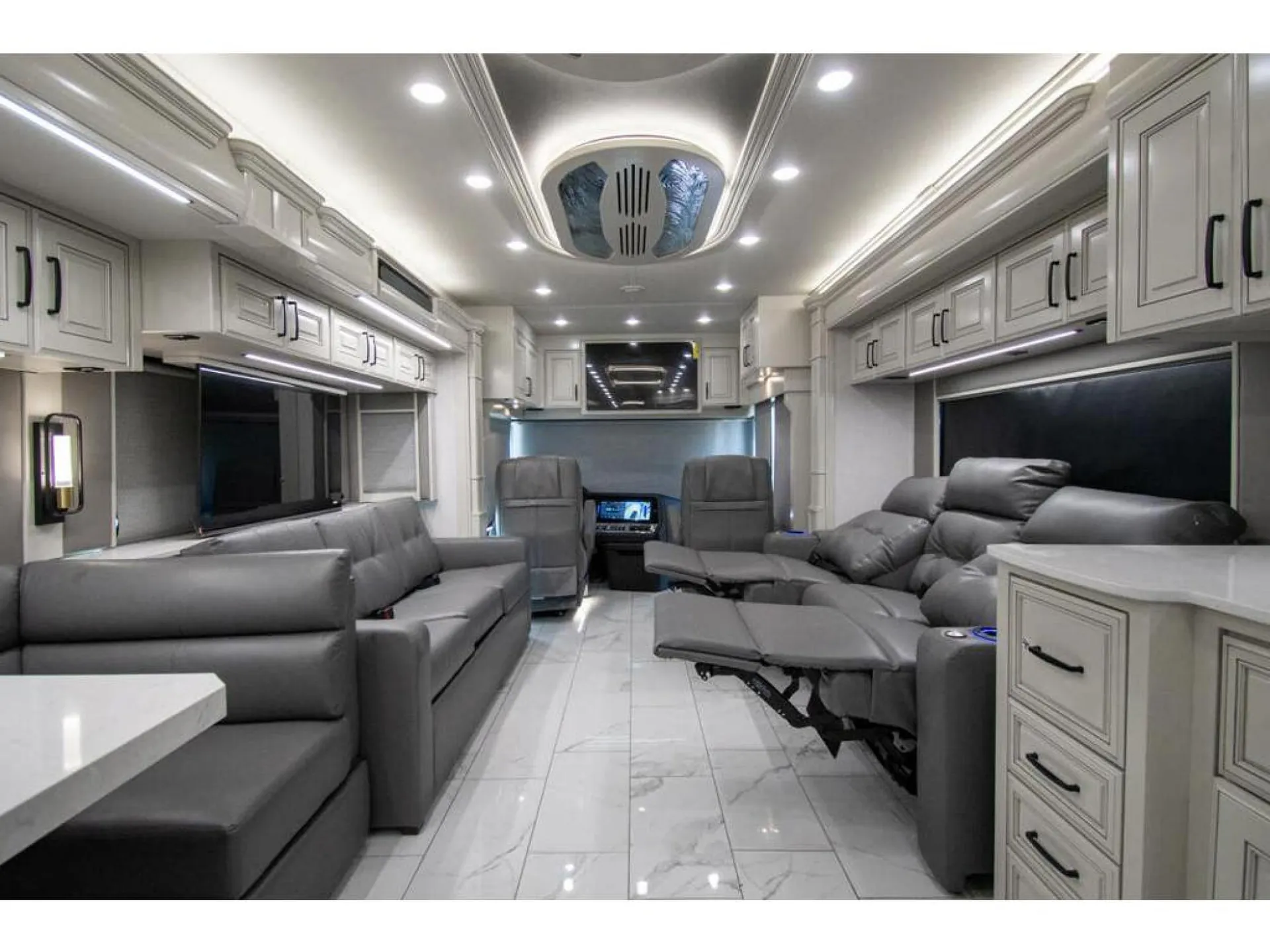 2026 American Coach American Dream 45A — Wide living area with sofas and recliners facing a dashboard and driver seats at the front