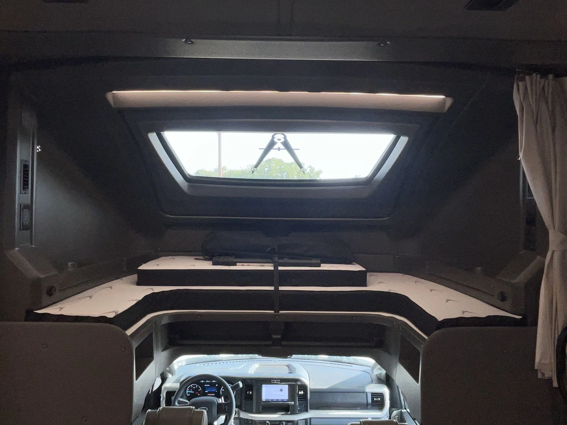 2027 Grand Design Lineage Series F 31ZW — Over-cab sleeping platform above the motorhome cockpit with mattress, skylight, and dashboard below