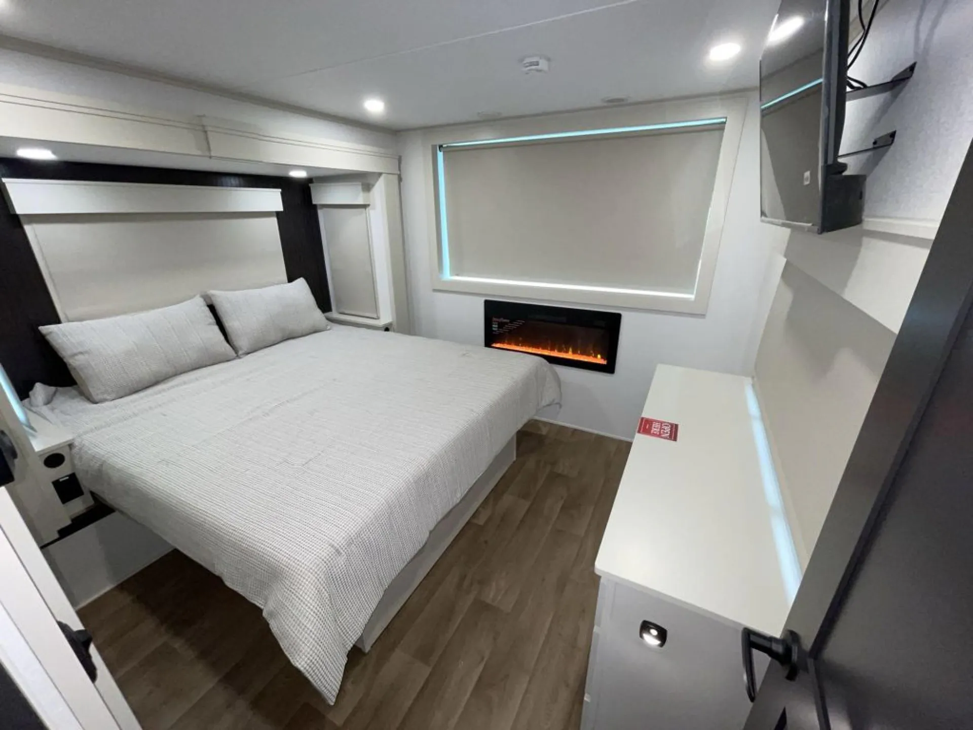 2026 Grand Design Foundation 42GD — Destination trailer bedroom with made bed, dresser, window shade, wall-mounted television, and electric fireplace