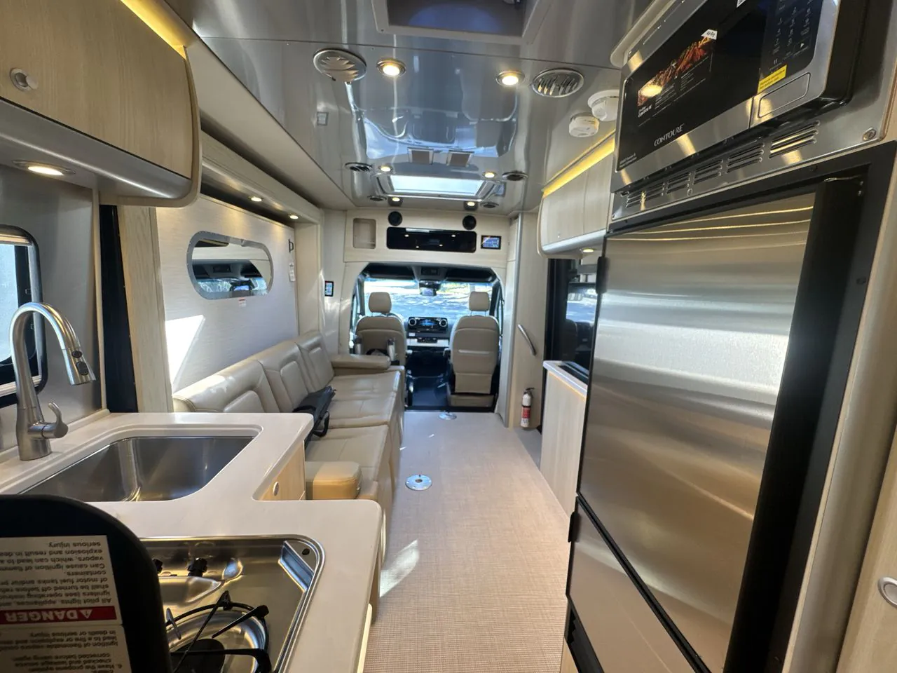 2026 Airstream Atlas Murphy Suite — Van interior overview showing the kitchen galley, lounge sofa, refrigerator, and driver cockpit